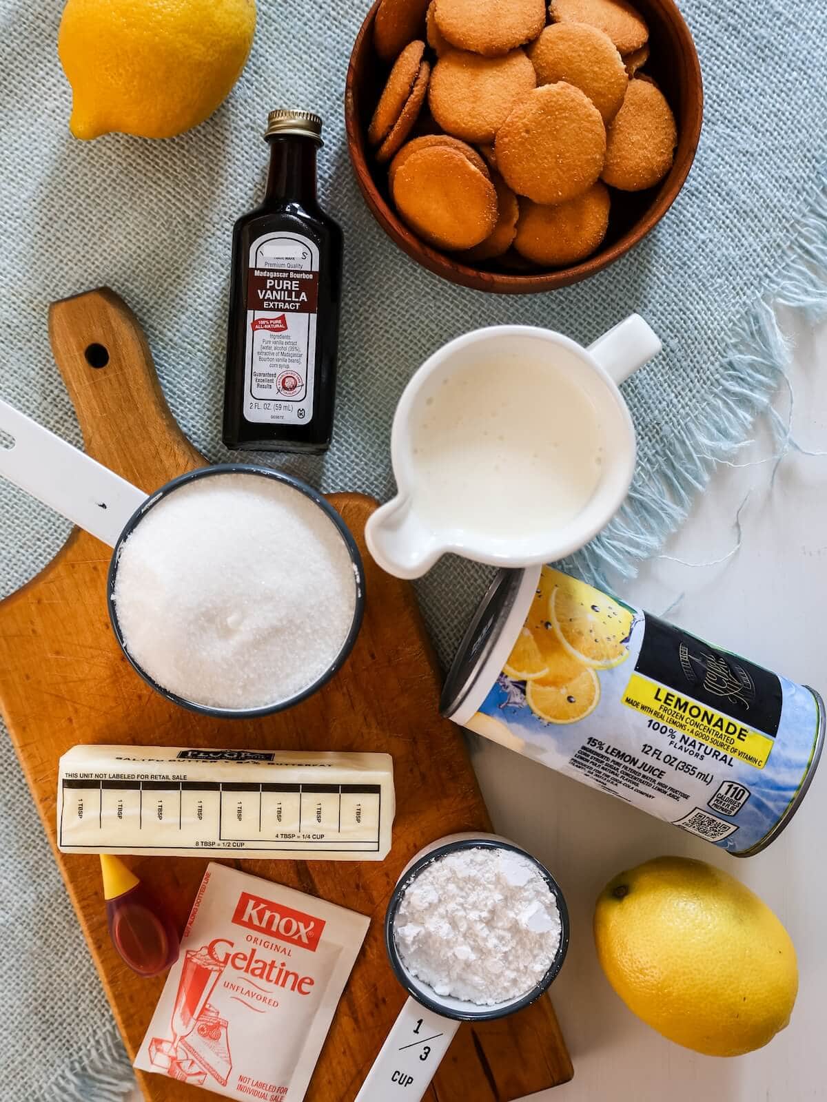 Ingredients for lemon icebox pie including lemonade, cream, sugar, butter, gelatine, food coloring, cookies, and confectioners' sugar.