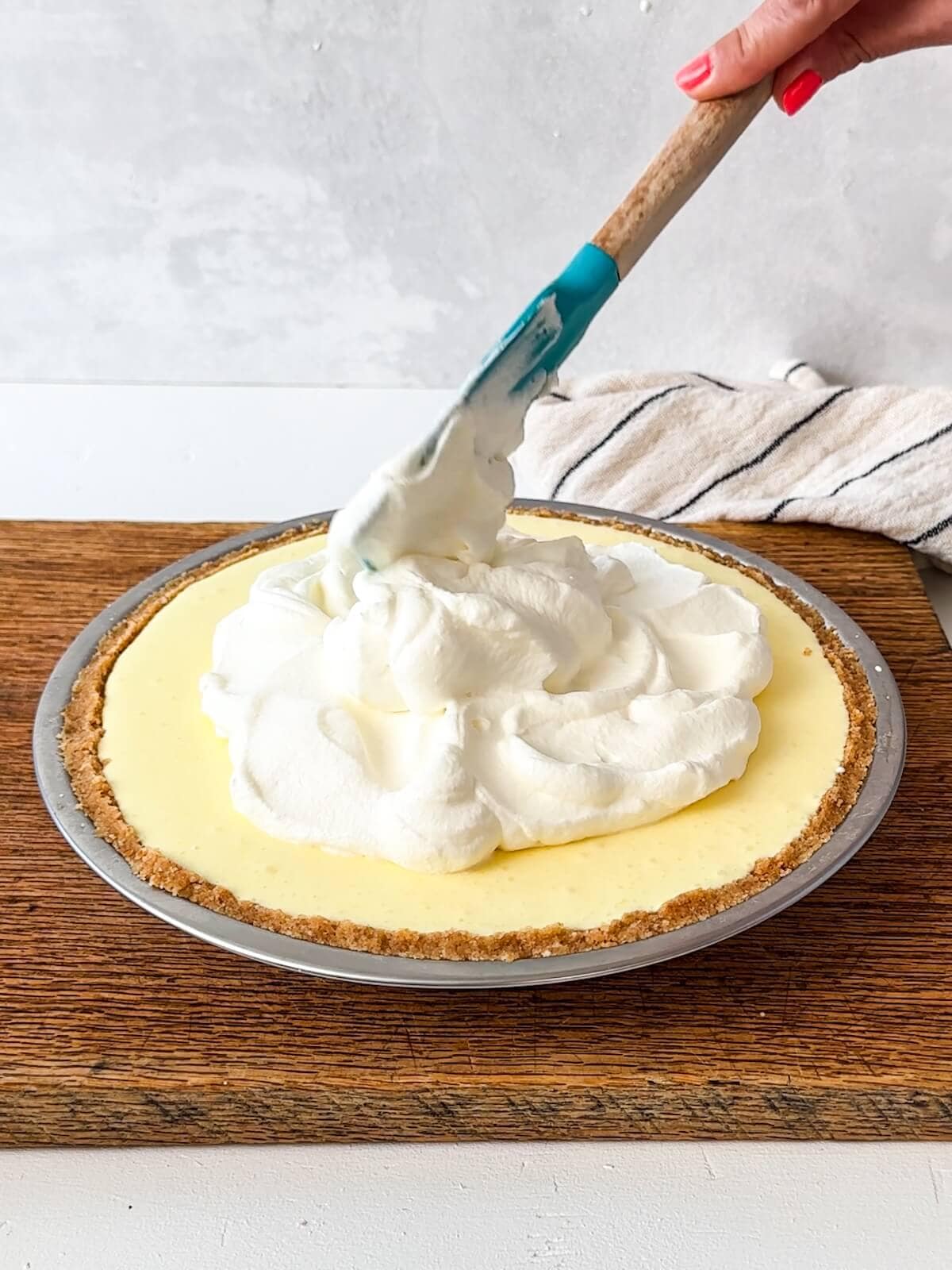 Adding whipped cream to the top of a lemon fluff pie.