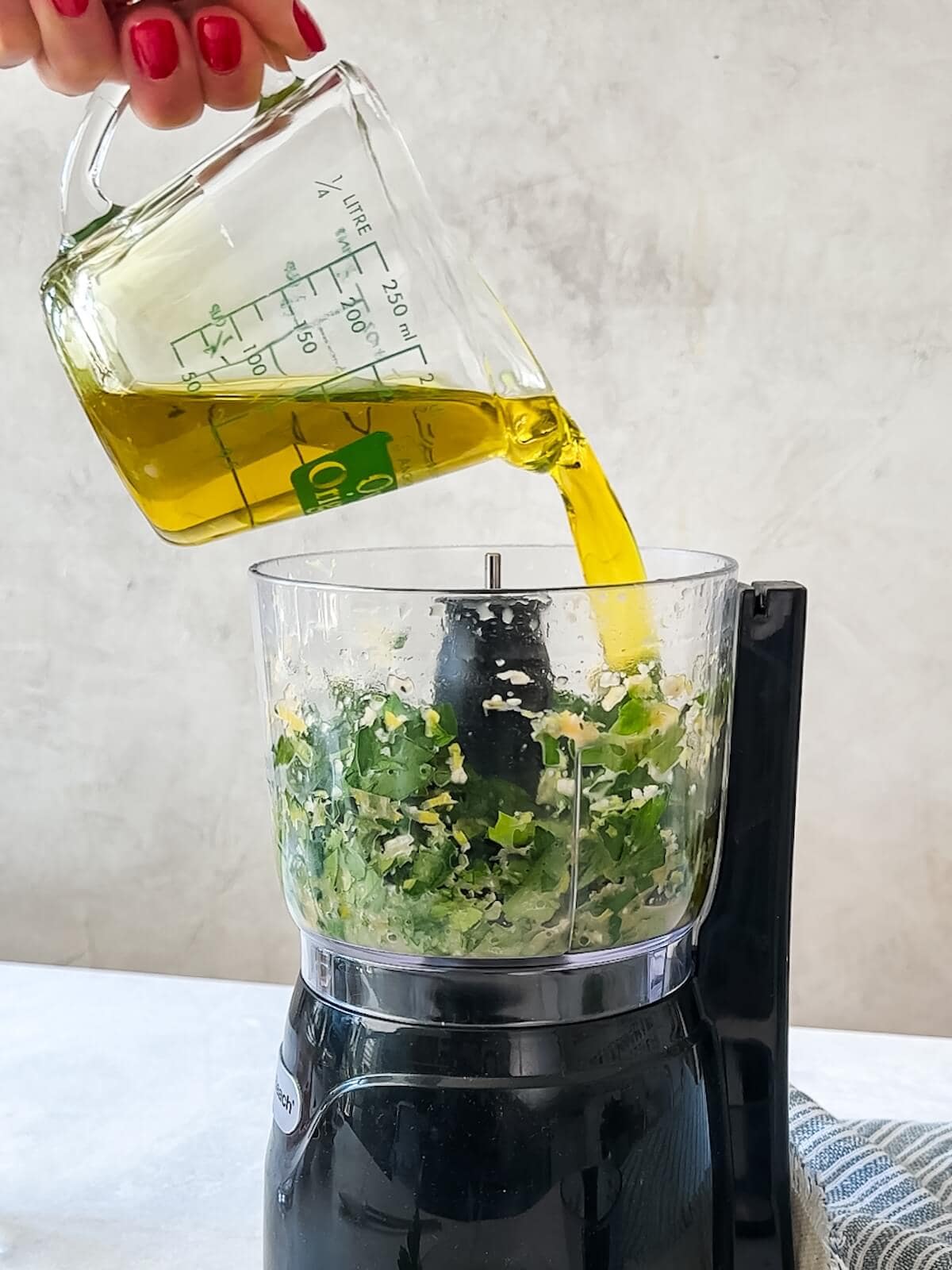 adding oil to a mini food processor full of salsa verde ingredients.