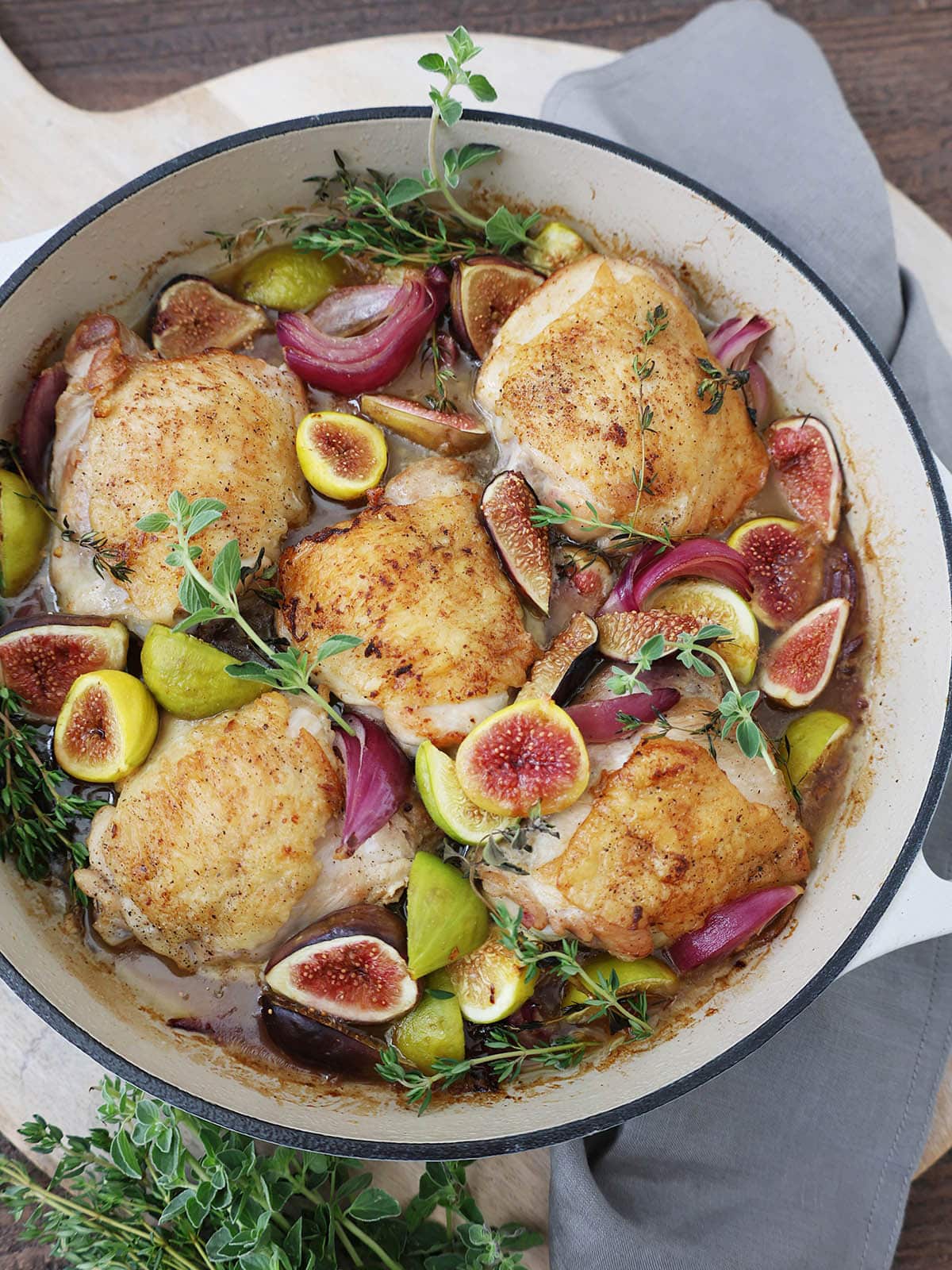 braised chicken thighs in a white skillet with honey, figs, and herbs.