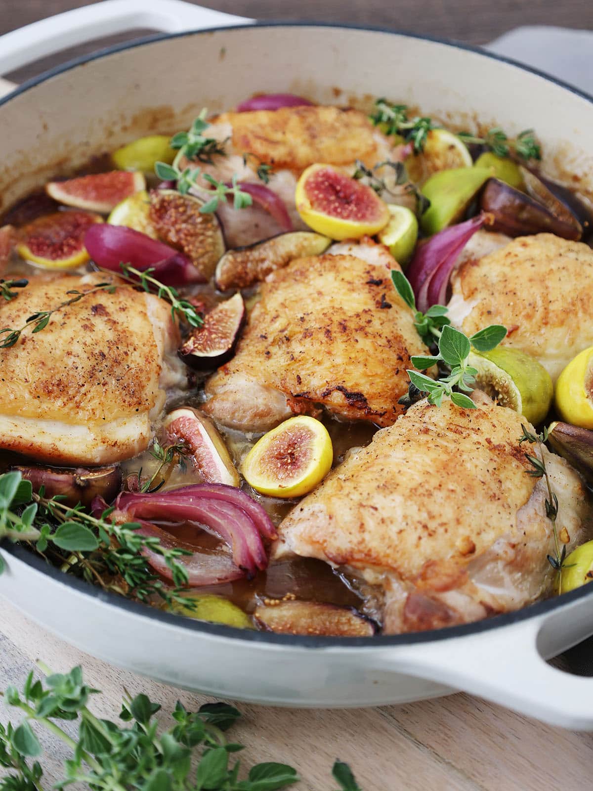 braising chicken with honey and figs in a white skillet.