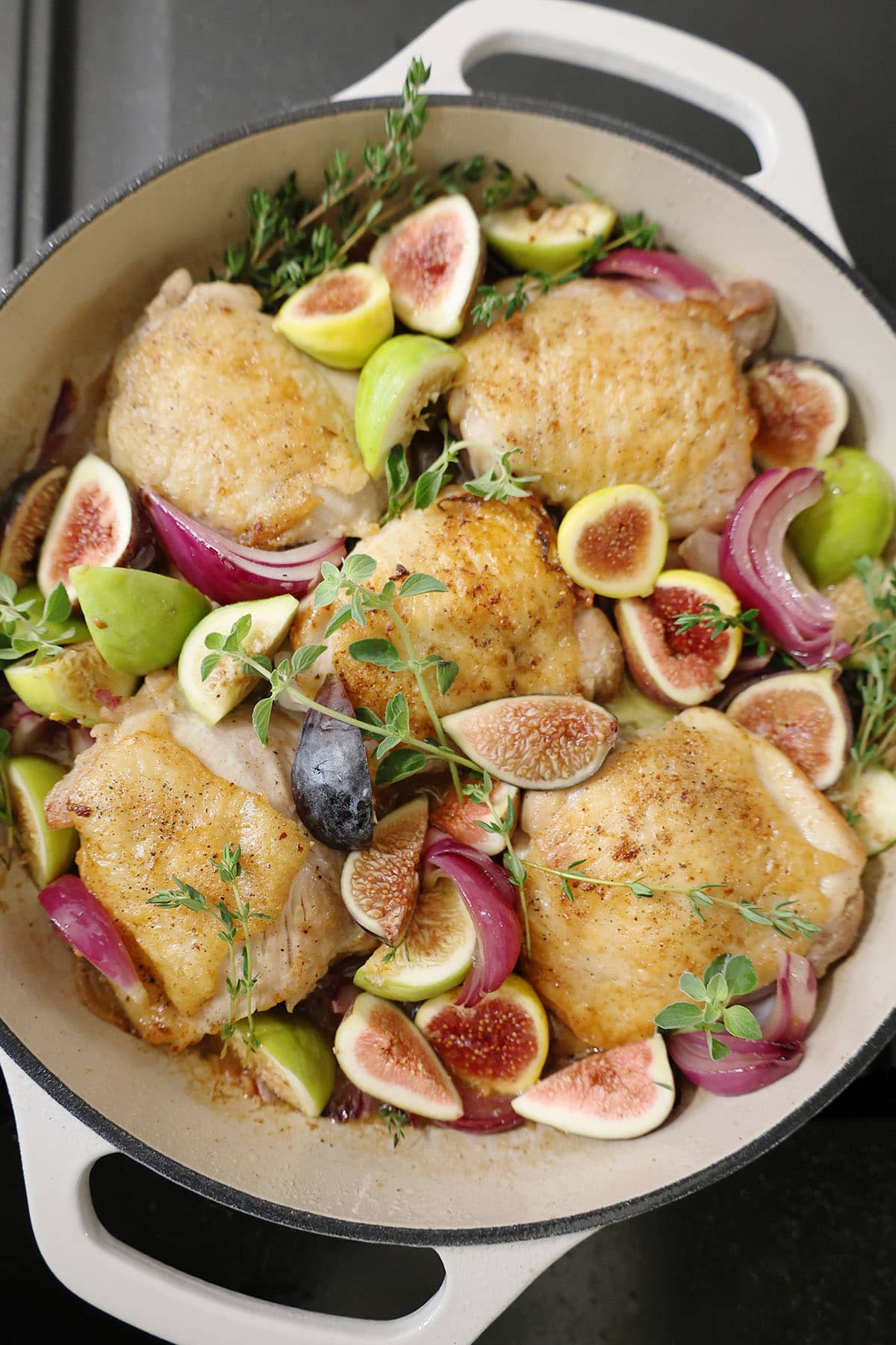 chicken, figs, honey, herbs, and red onions in a white skillet ready to go in the oven.