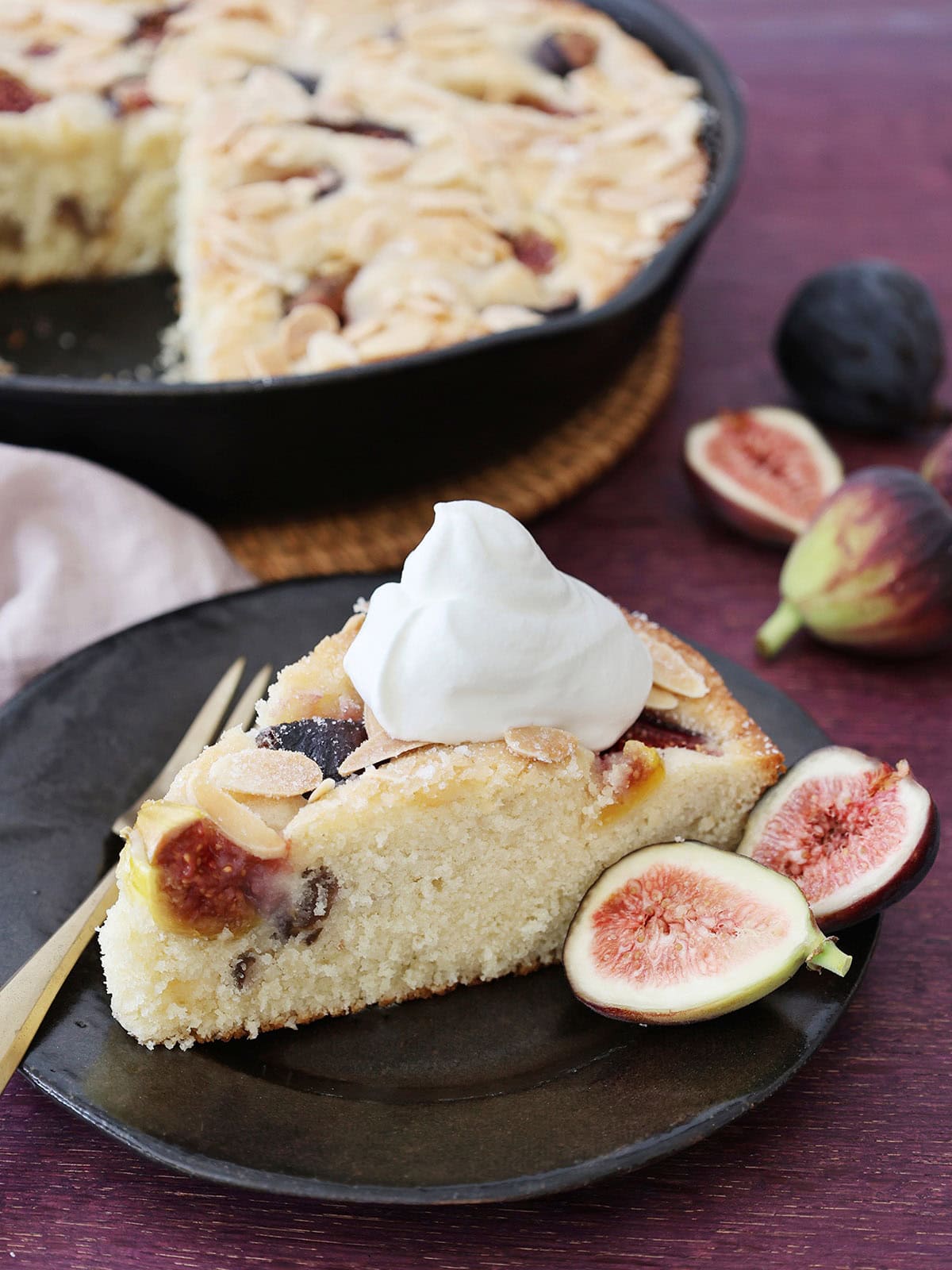 fig almond snack cake on a dark plate with fresh figs and whipped cream.
