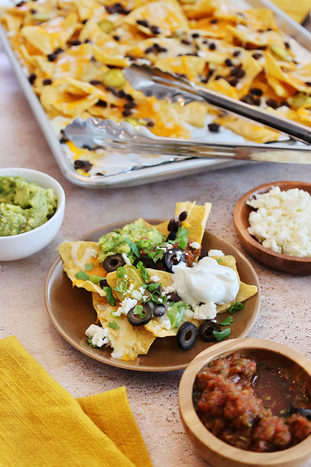 nachos made on a sheet pan served on a brown plate with toppings.