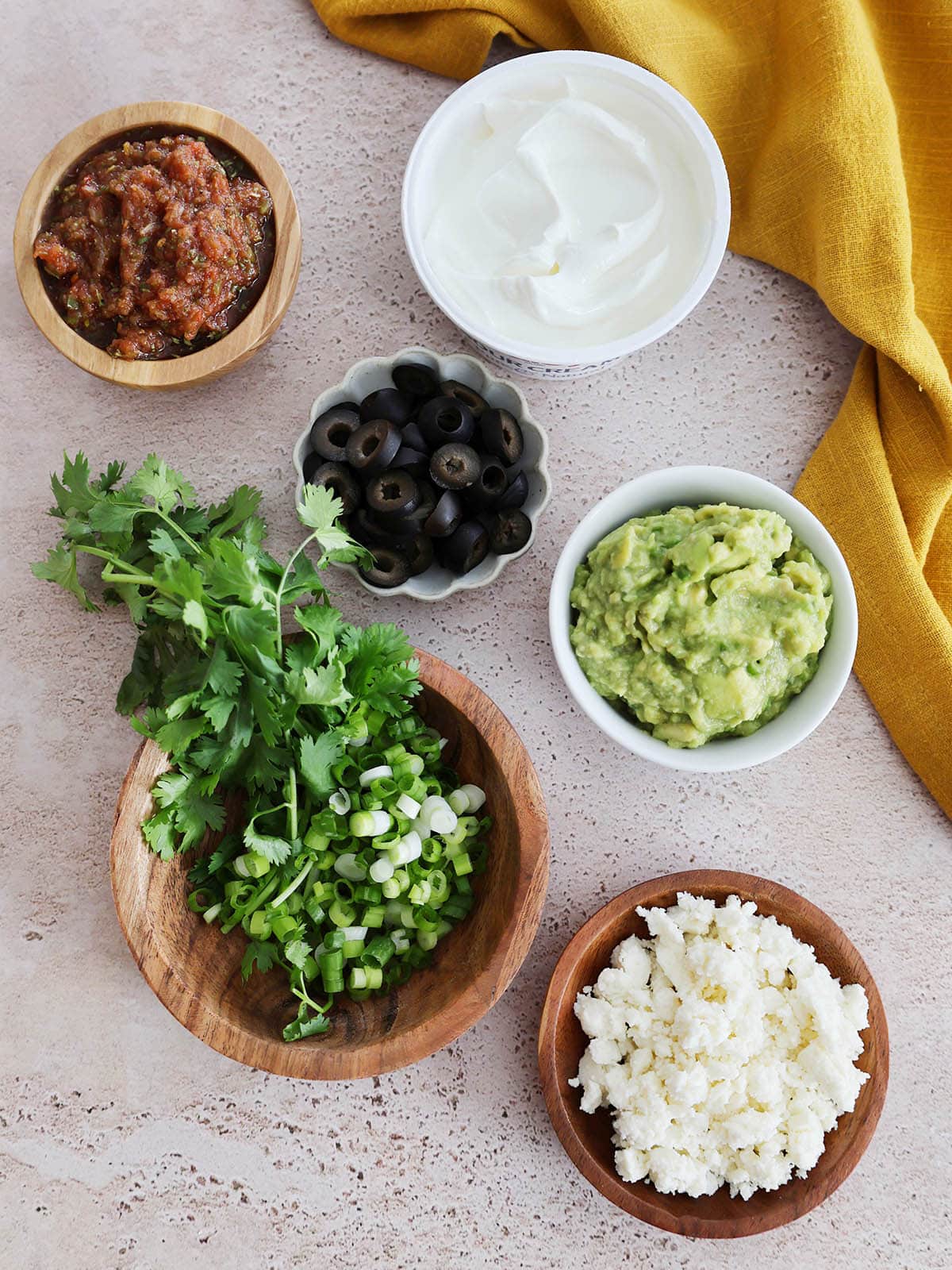 Toppings for oven baked nachos including sour cream, olives, guacamole, cotija cheese, herbs, and salsa.