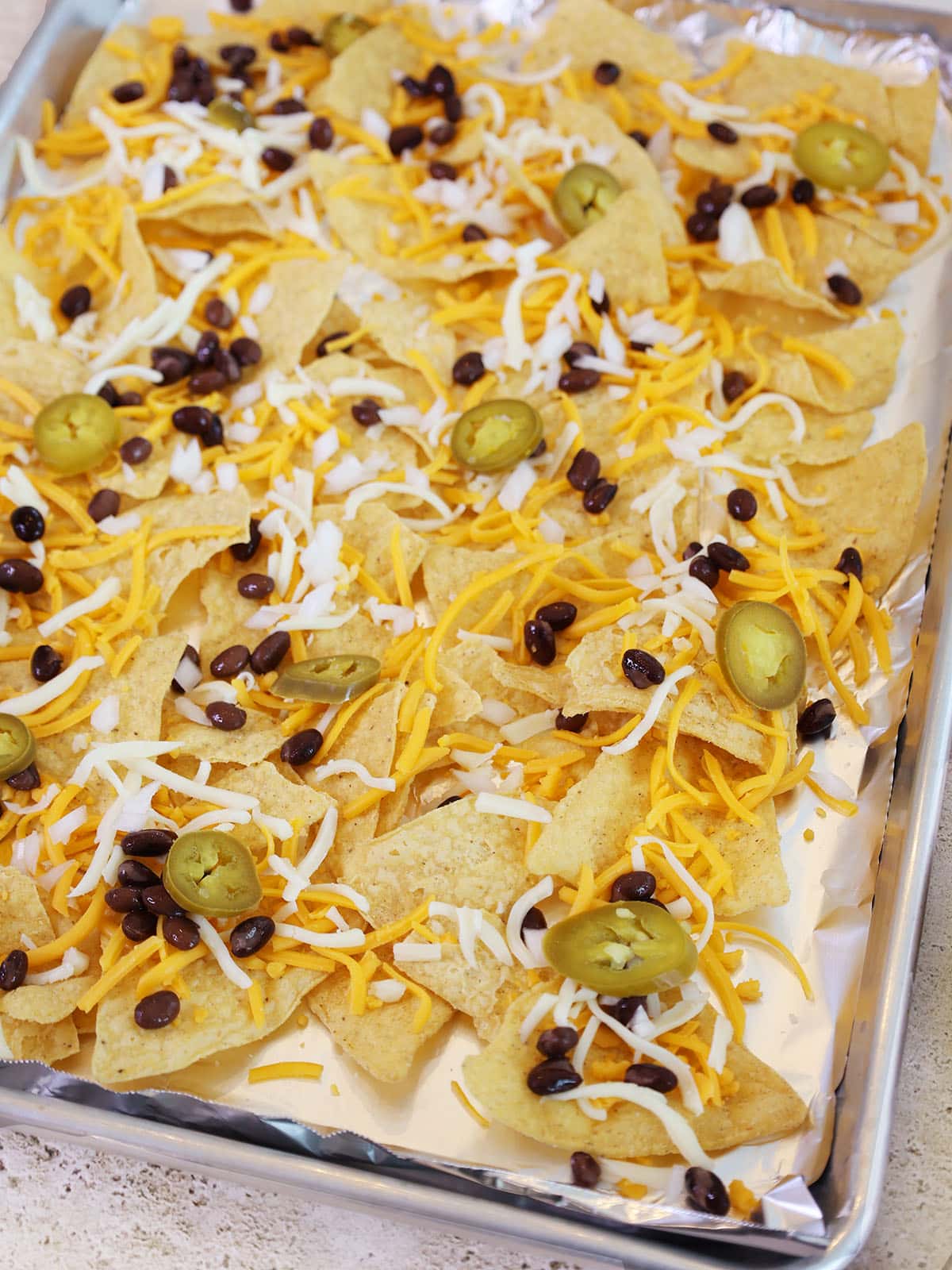 the first layer of chips, cheese, beans, and jalapenos for making nachos in the oven.