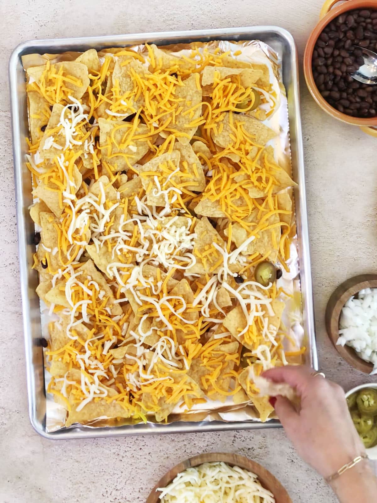 adding top layer of cheese to oven baked nachos before baking.