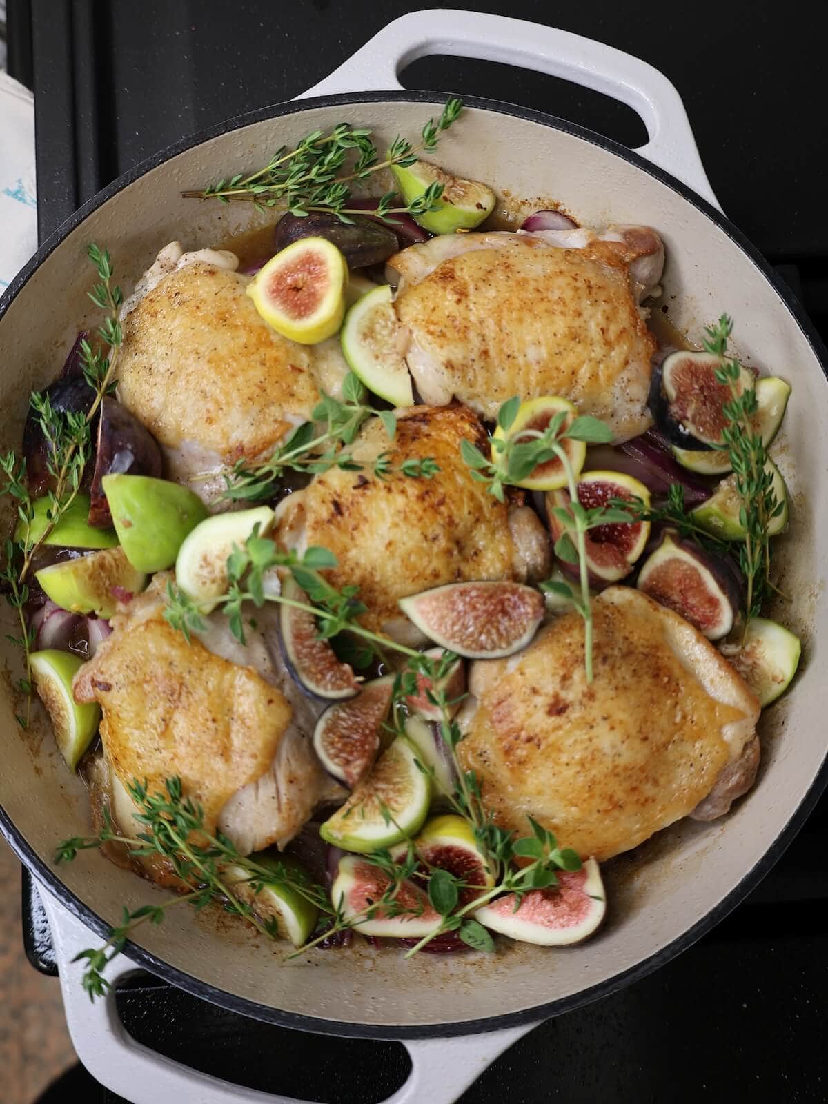 chicken thighs, figs, herbs, and sauce in a skillet ready to roast.