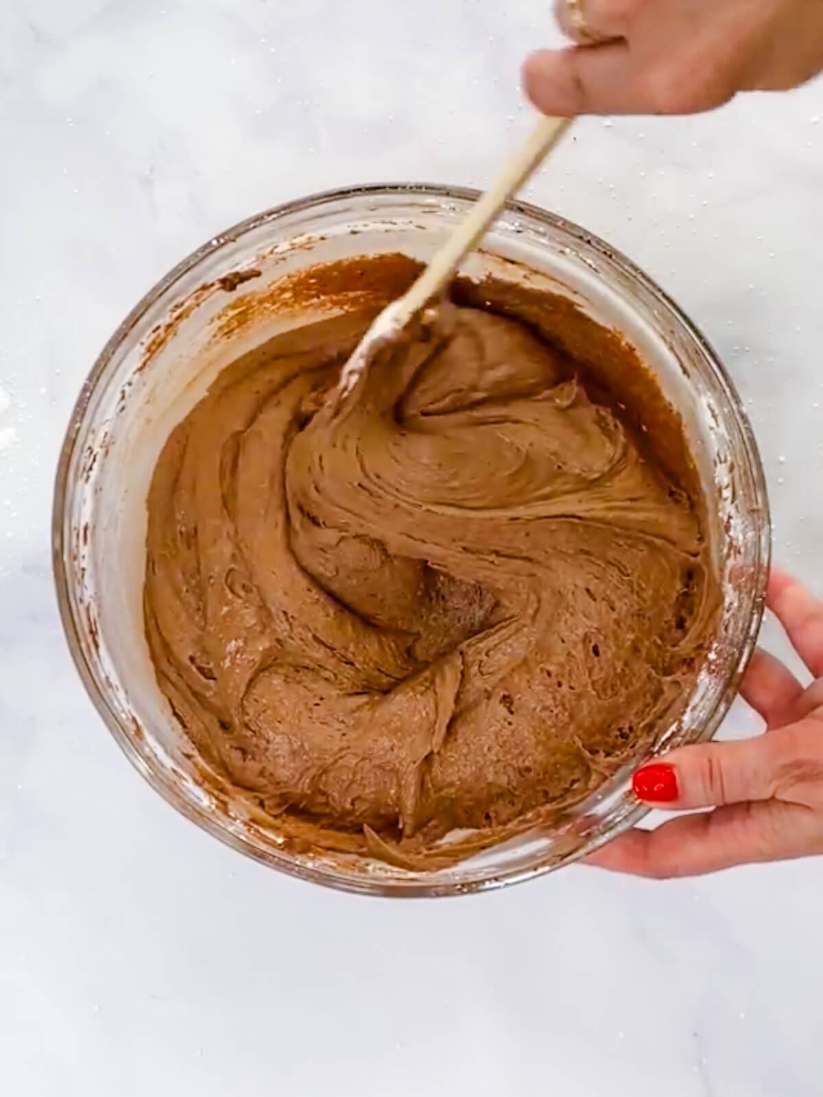 Using a spatula to scrape the sides of the frosting bowl.