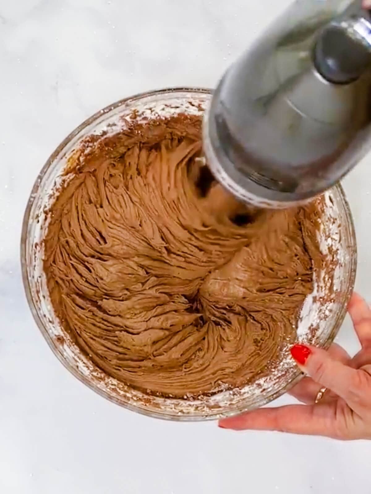 Using a hand mixer to combine buttercream ingredients.