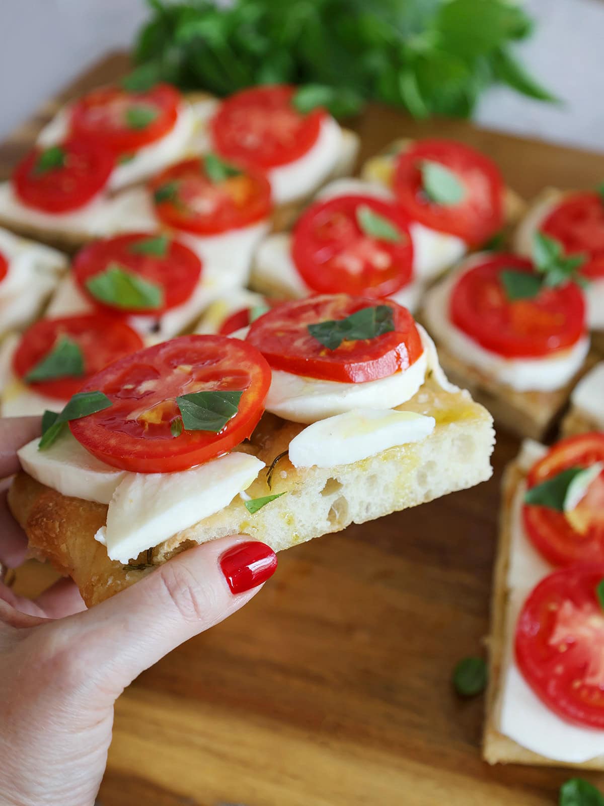 hand holding a piece of caprese focaccia with red finger nail.