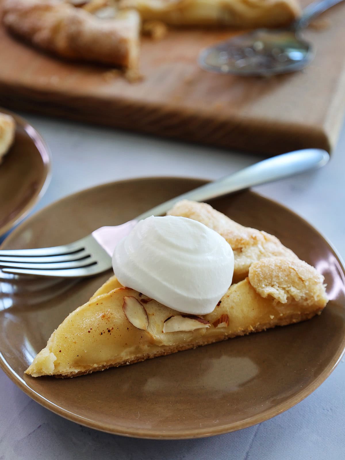 slice of rustic apple tart recipe with almond frangipane and a dollop of cream.