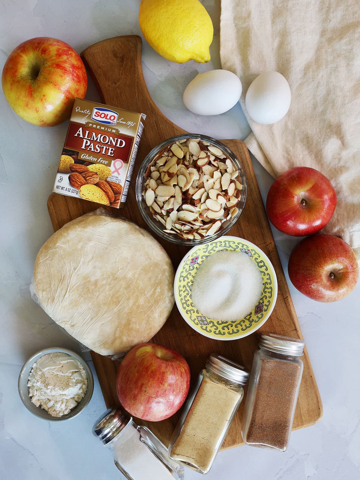 Ingredients for apple tart with frangipane including apples, sugar, pastry, spices, almonds, almond paste, lemon and egg.