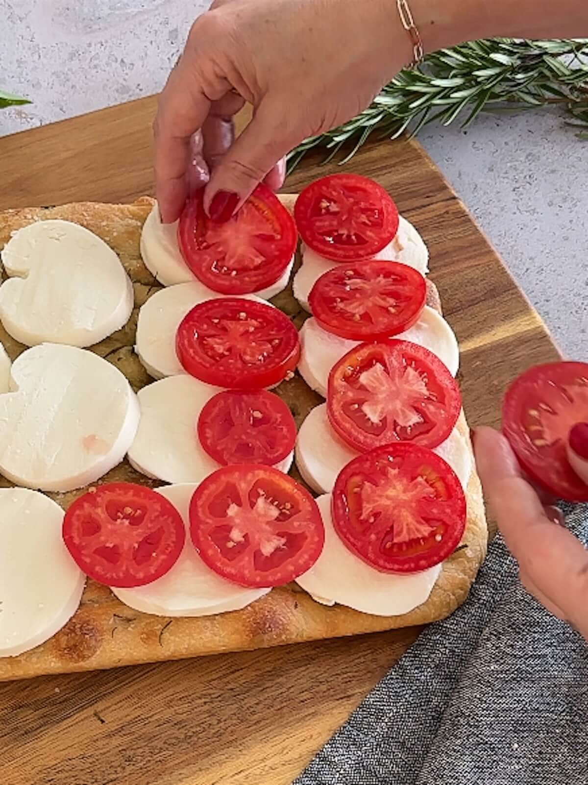 placing fresh tomato slices on caprese focaccia
