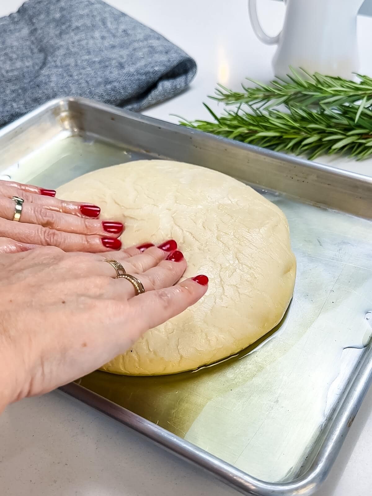 thawed pizza dough on a greased baking sheet with hands pressing dough.