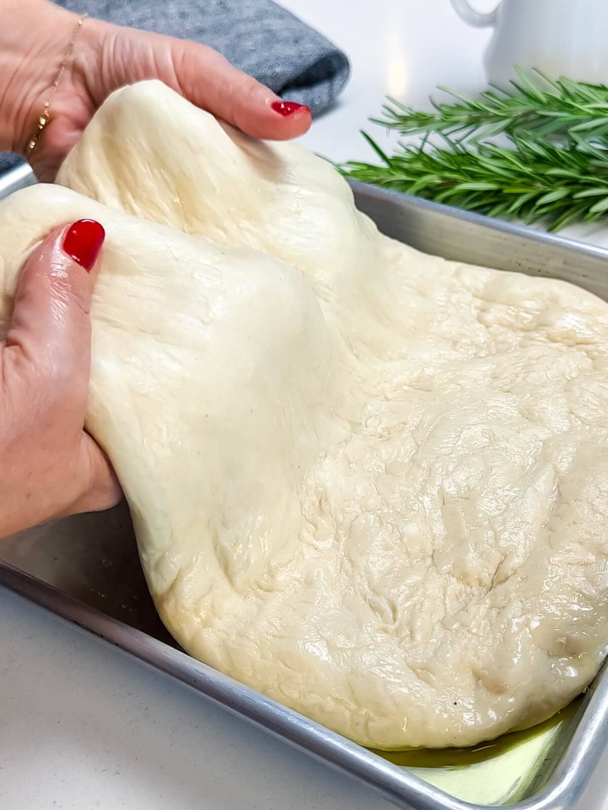 gently stretching pizza dough to form into focaccia in a pan