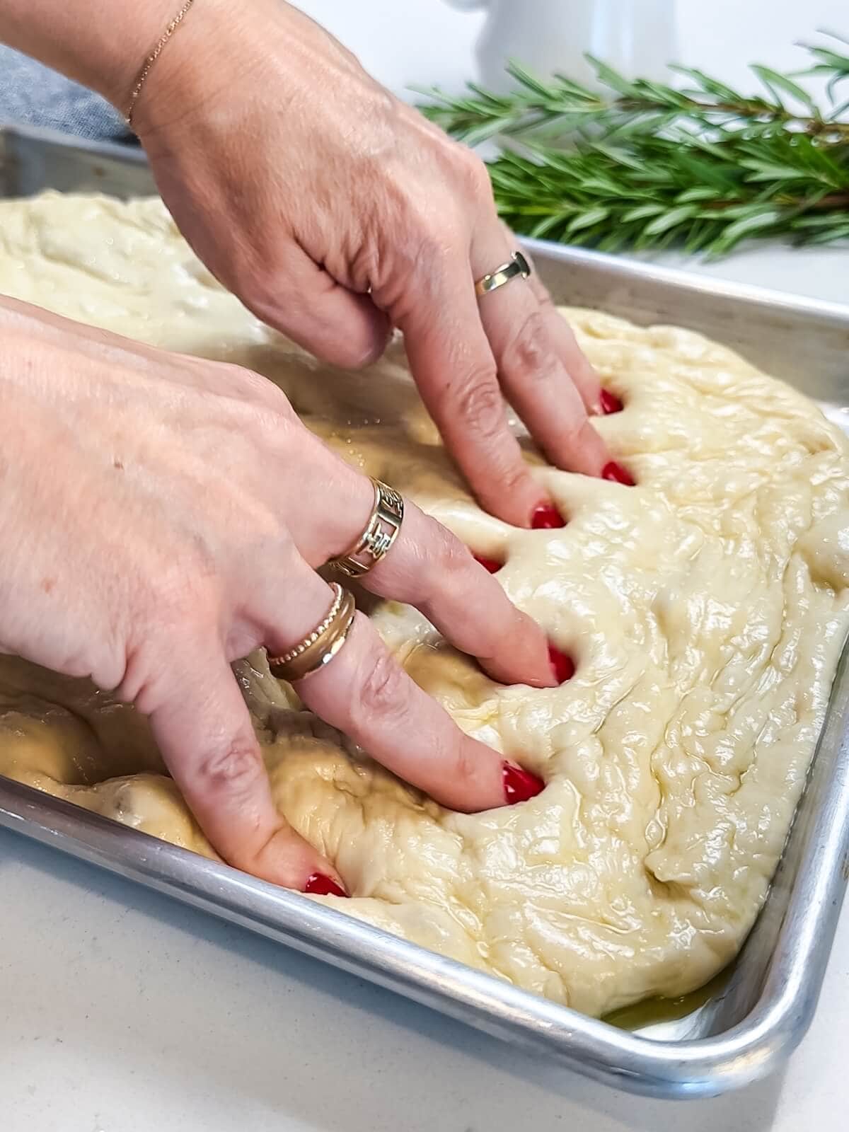 using fingers to dimple focaccia in a pan before baking.