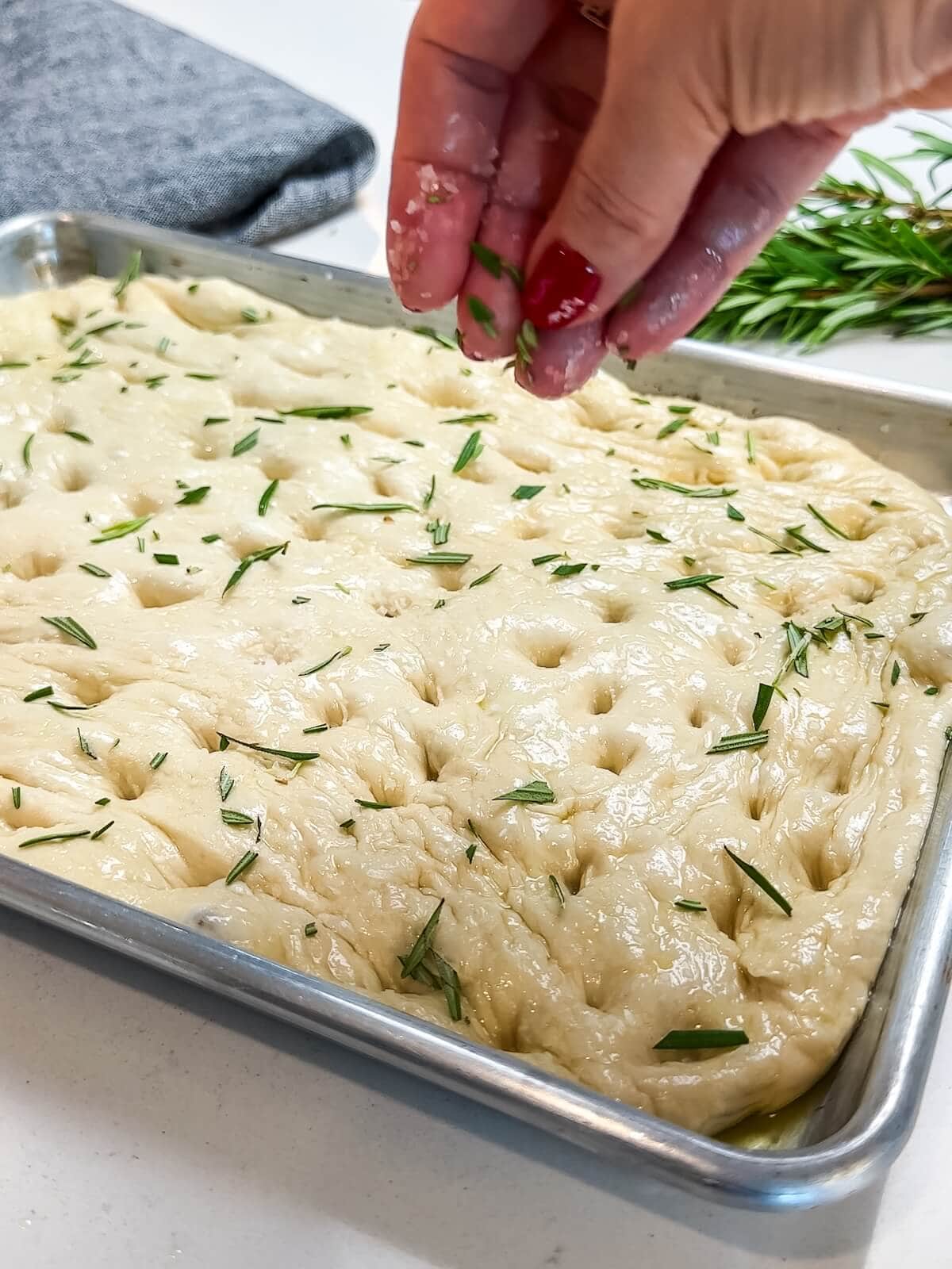 sprinkling focaccia dough with salt and rosemary before baking.