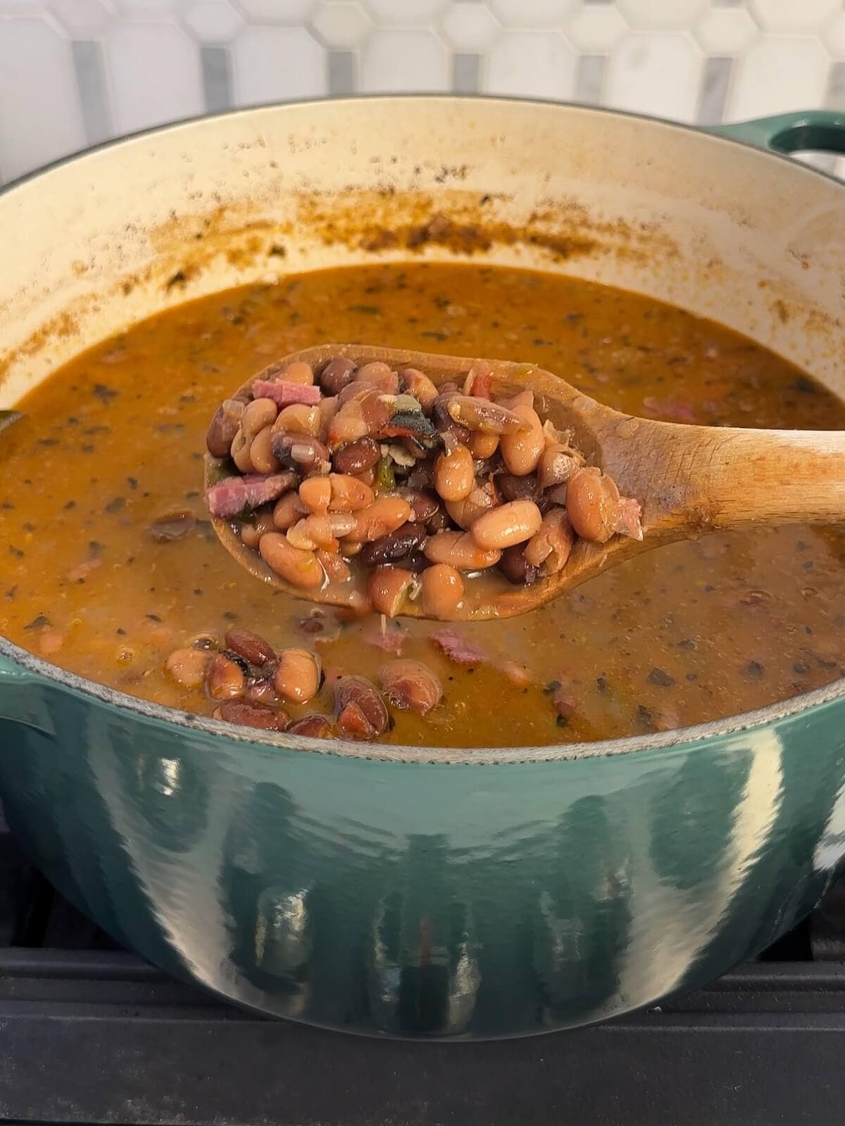 simmered charro beans in a dutch oven on the stove, spoon holding some up.