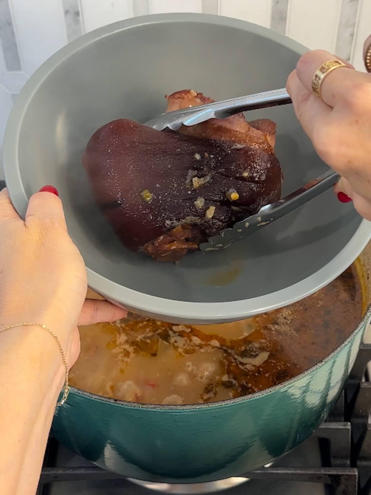 removing ham hock with tongs from simmering charro beans.