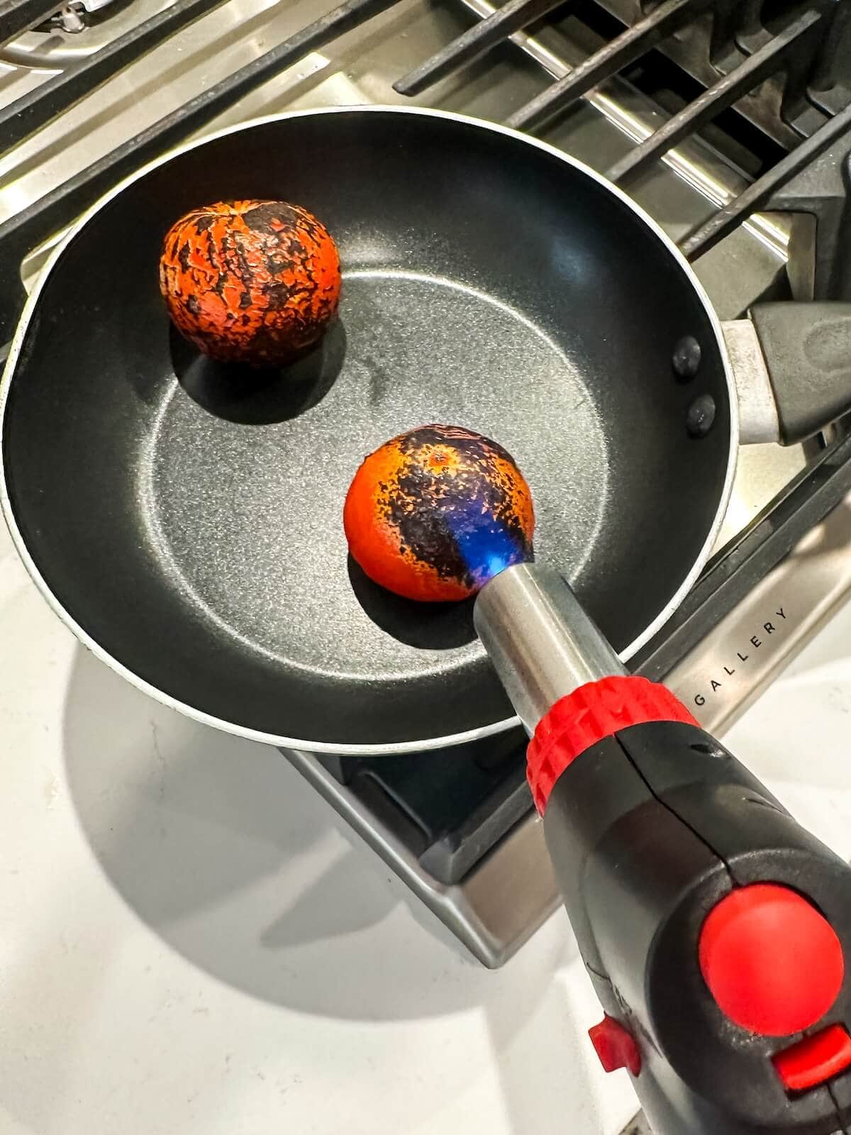 charring tomatoes with a kitchen torch in a pan