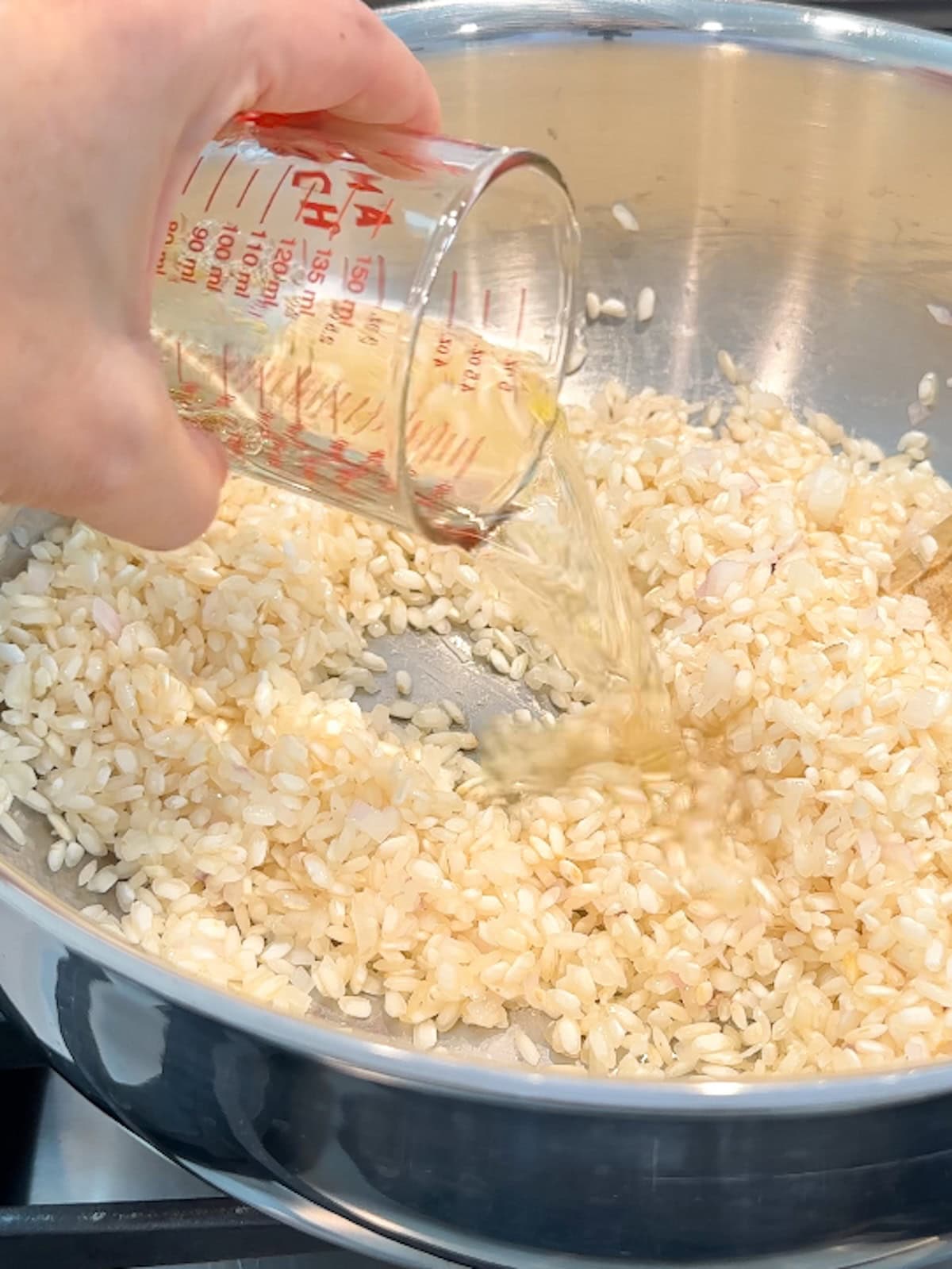 Adding white wine to risotto recipe in a pan.