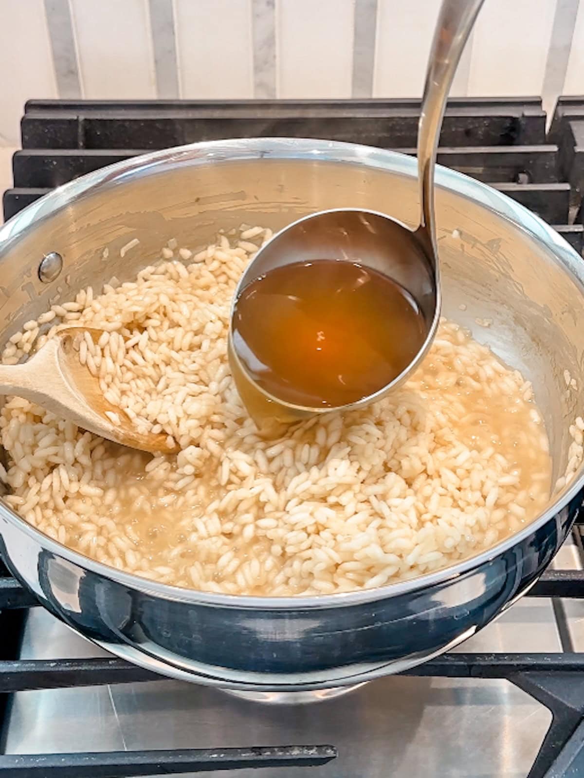 Adding broth 1 cup at a time to cooking risotto.