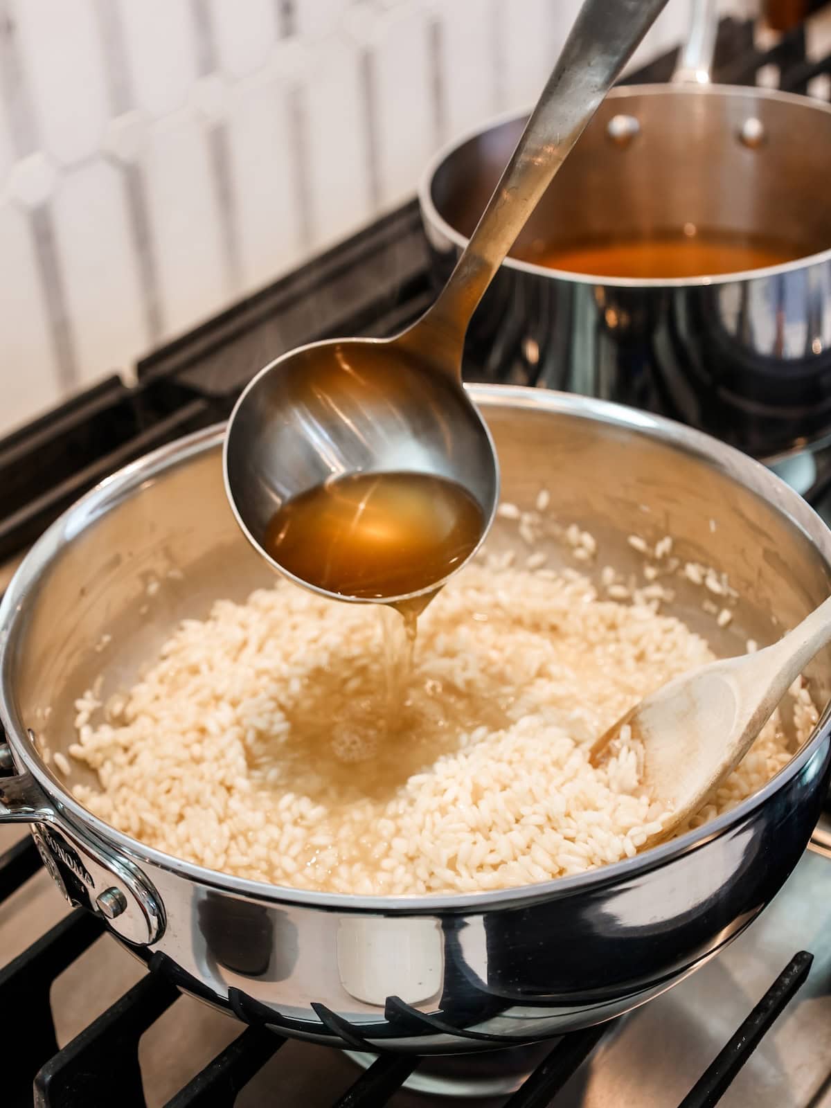 pan of broth on stove next to risotto to add hot broth to the rice.