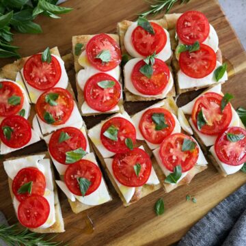 feature image of caprese focaccia cut into portions on a cutting board.