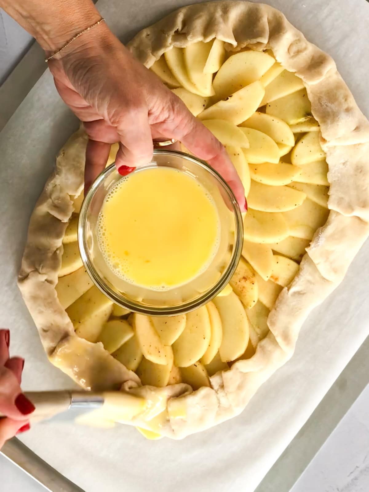 brushing egg wash on the crust of an apple almond tart.