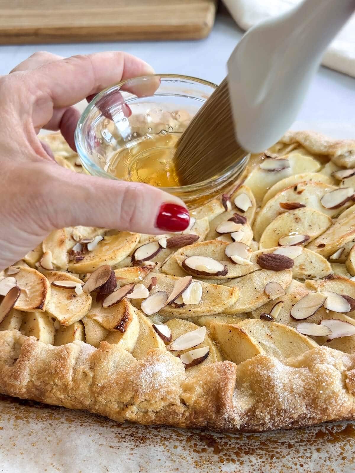 brushing melted honey over apples on a baked tart.