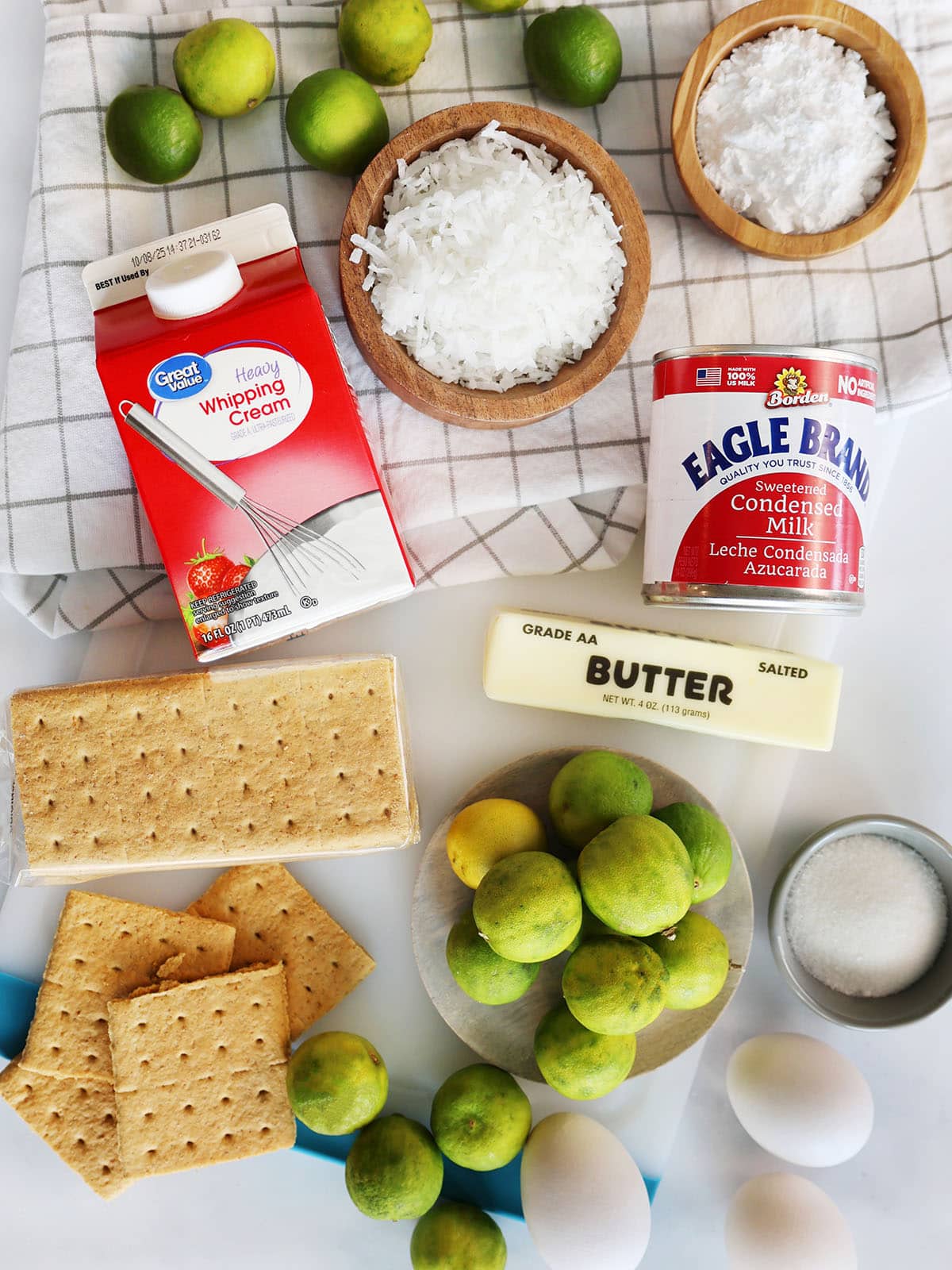 Ingredients for coconut key lime pie bars including key limes, sugar, eggs, graham crackers, cream, sweetened condensed milk, coconut, confectioners sugar, and butter.