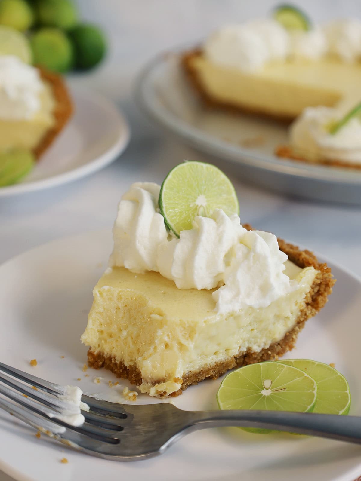 A slice of Key lime pie on a white plate with a bite removed.