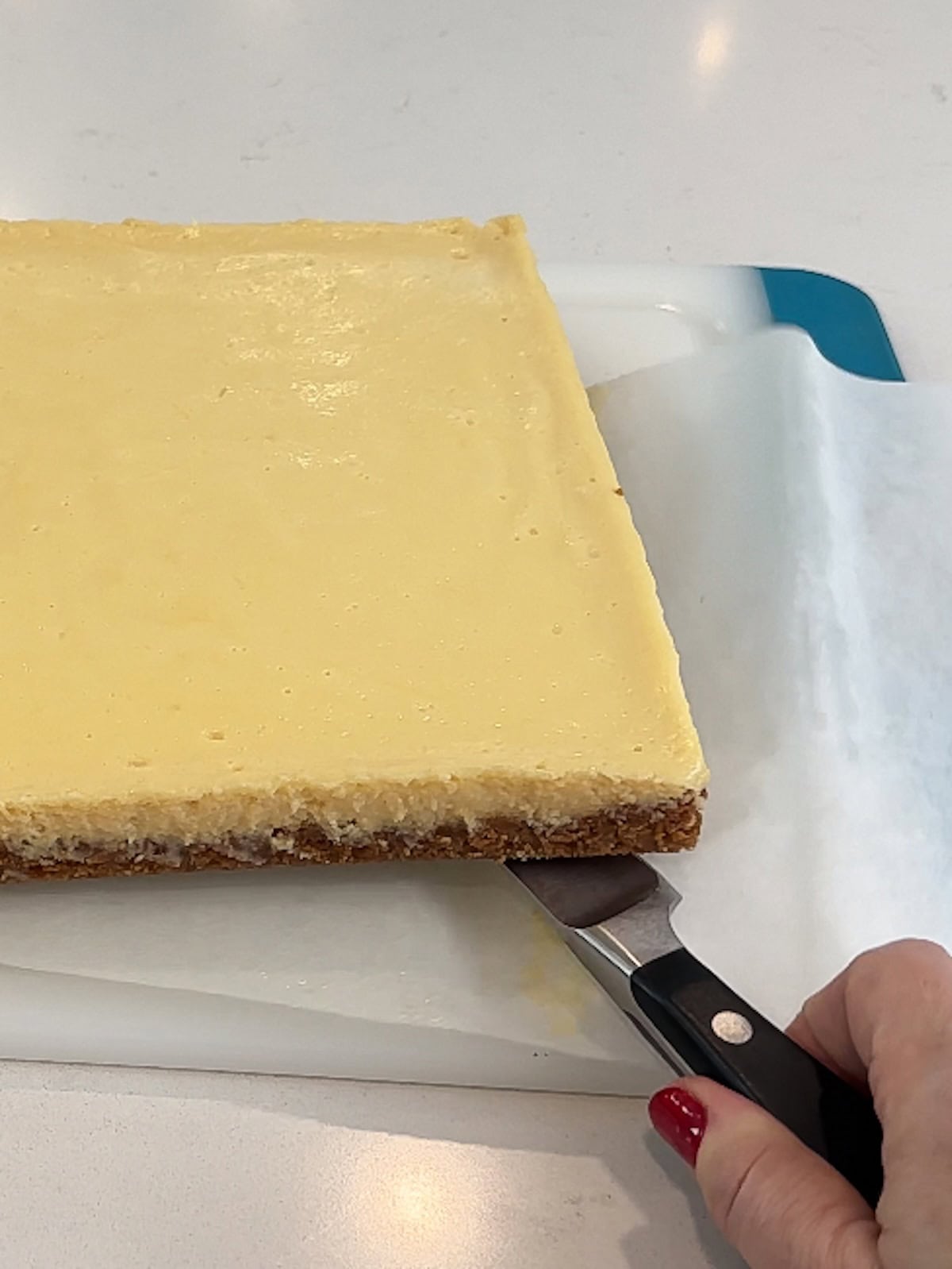 Removing cooked key lime bars from parchment to cut and serve.