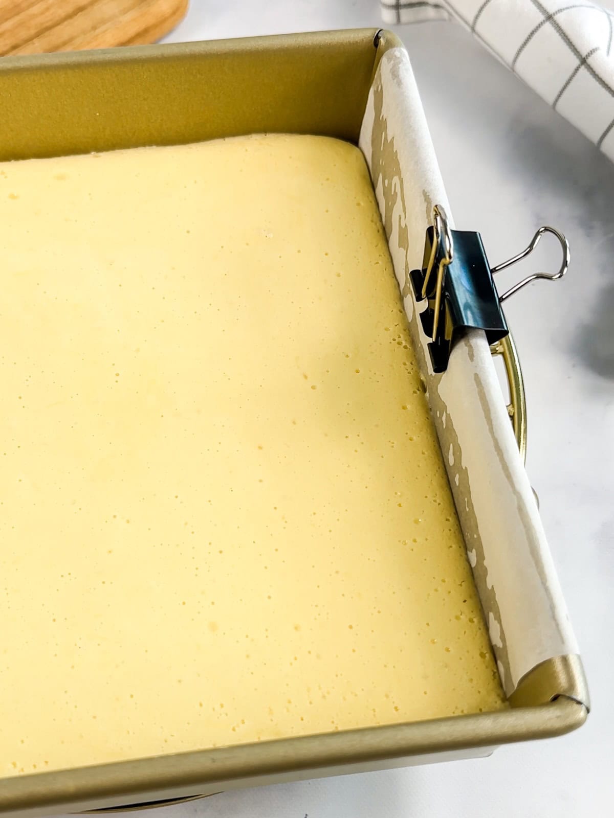 Cooking key lime bars with a metal clip on the pan to hold down the parchment paper flaps.