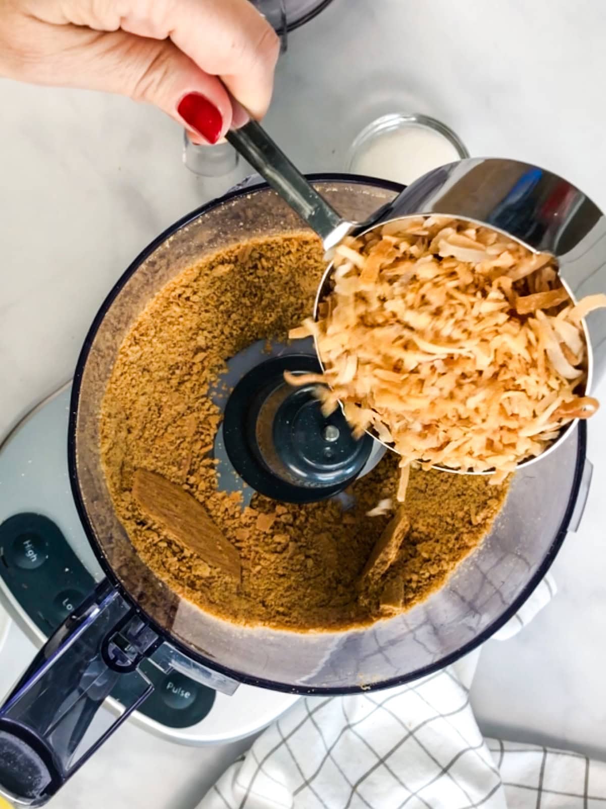 Adding toasted coconut to the graham cracker crust mixture in the food processor.