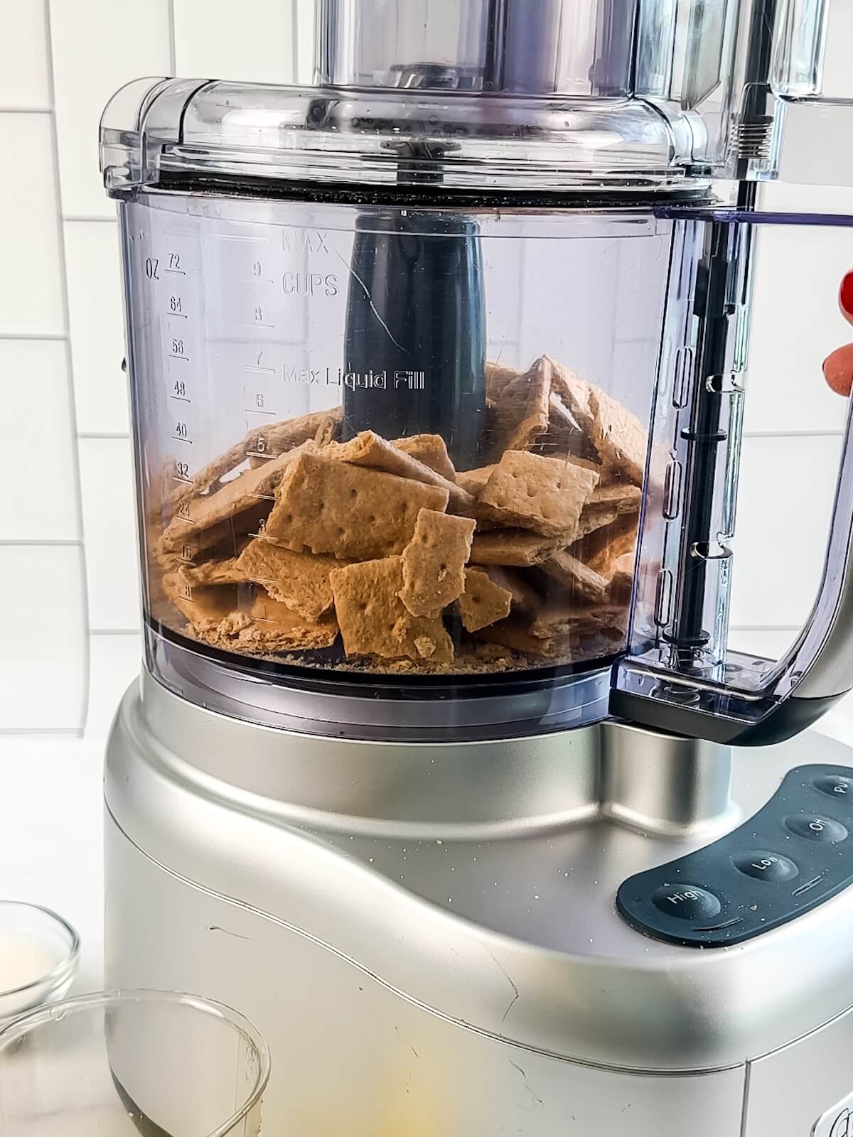 Broken graham crackers in a food processor, ready to grind into fine crumbs for crust.