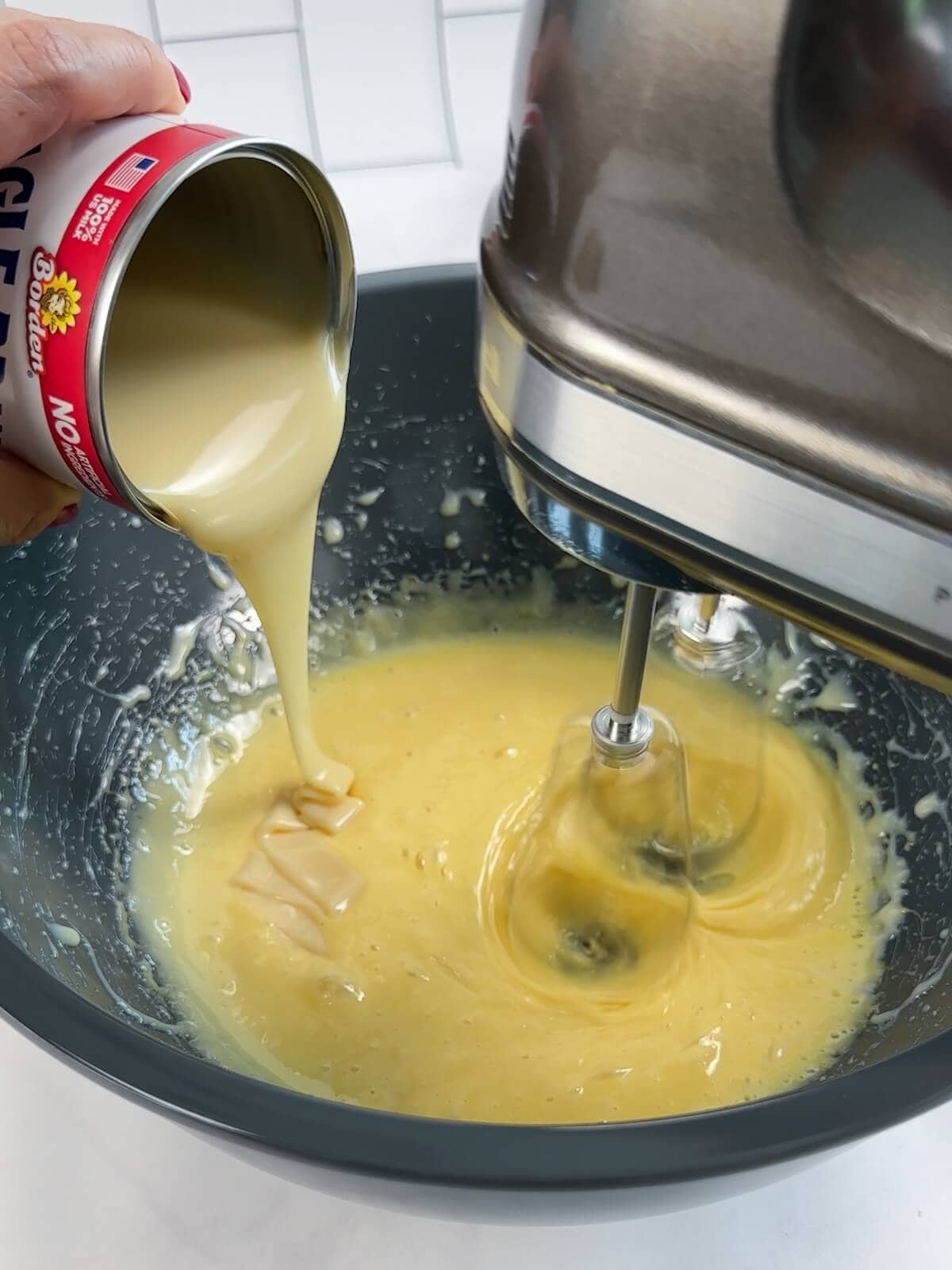 Adding sweetened condensed milk to key lime pie filling while mixer is running.
