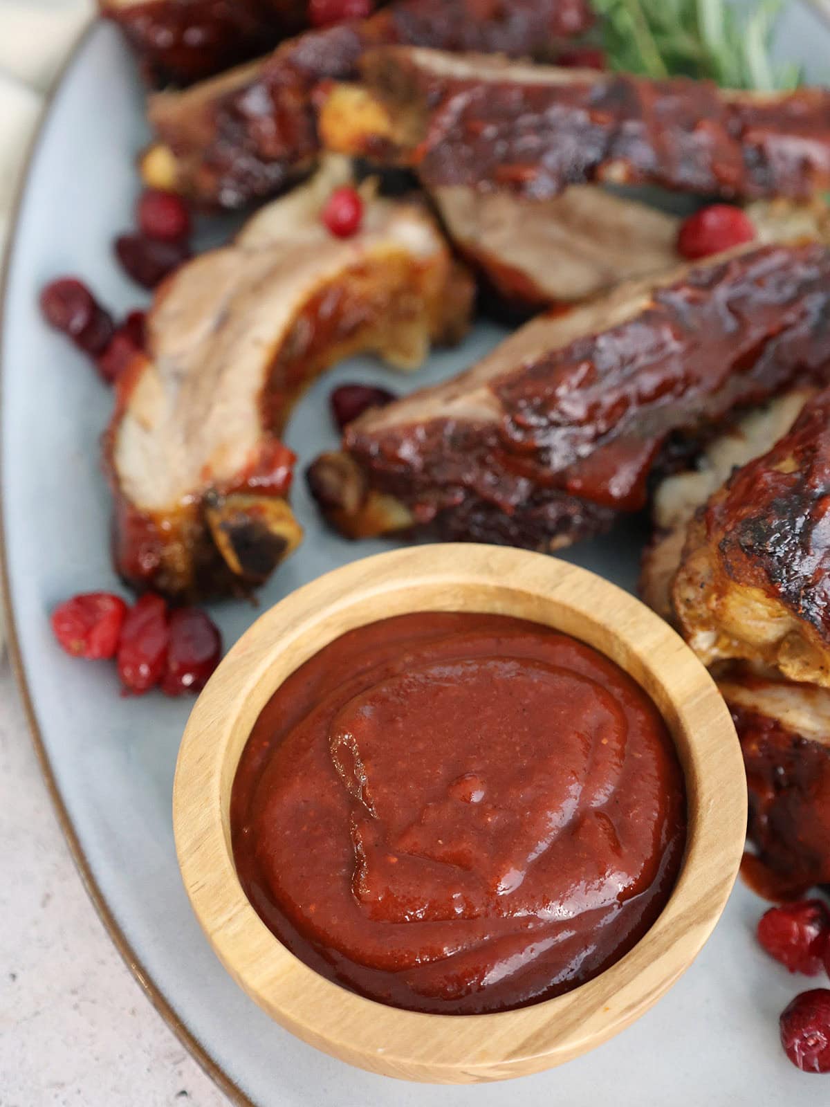 A small wooden bowl of cranberry bbq sauce next to some ribs.