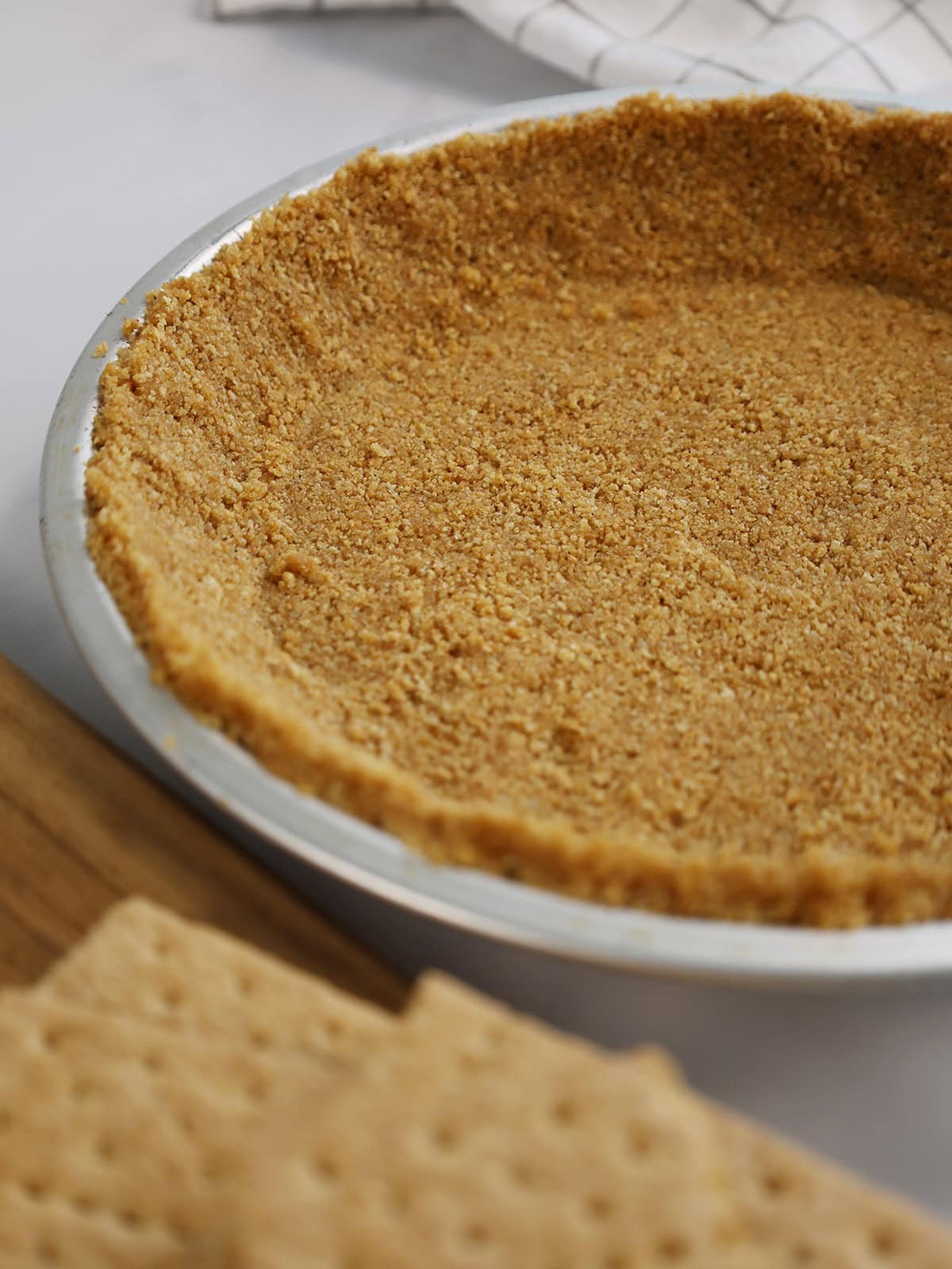 Graham cracker pie crust in a silver pie pan.