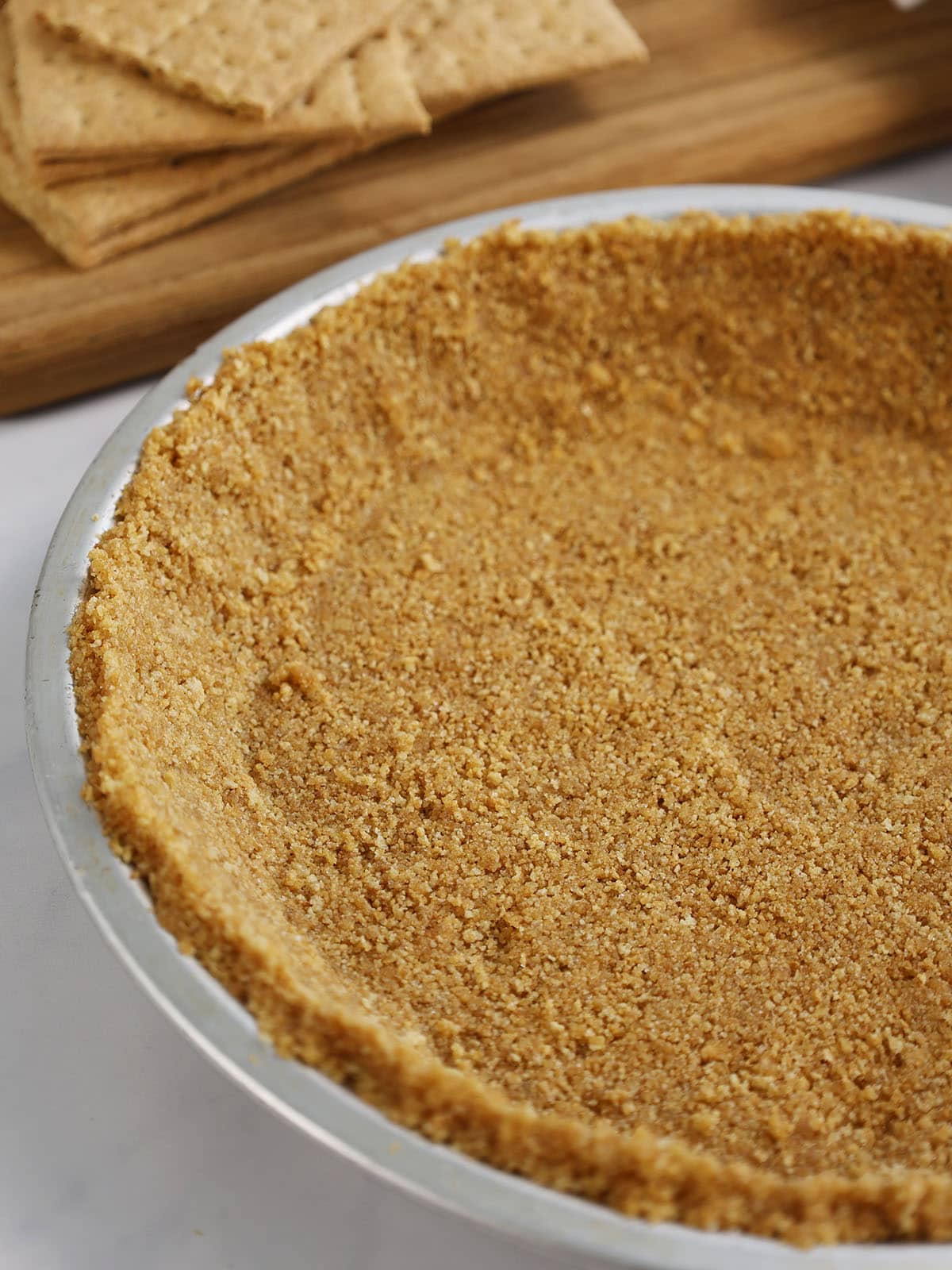 Close up of a graham cracker pie crust in a silver pie plate.