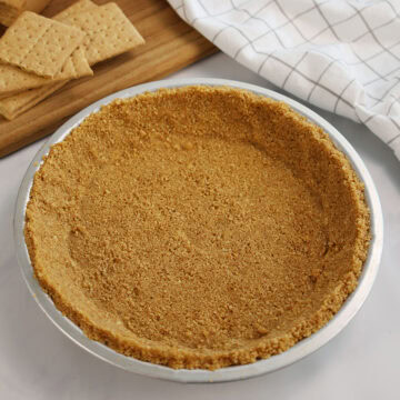 Graham cracker pie crust in a silver pie pan.
