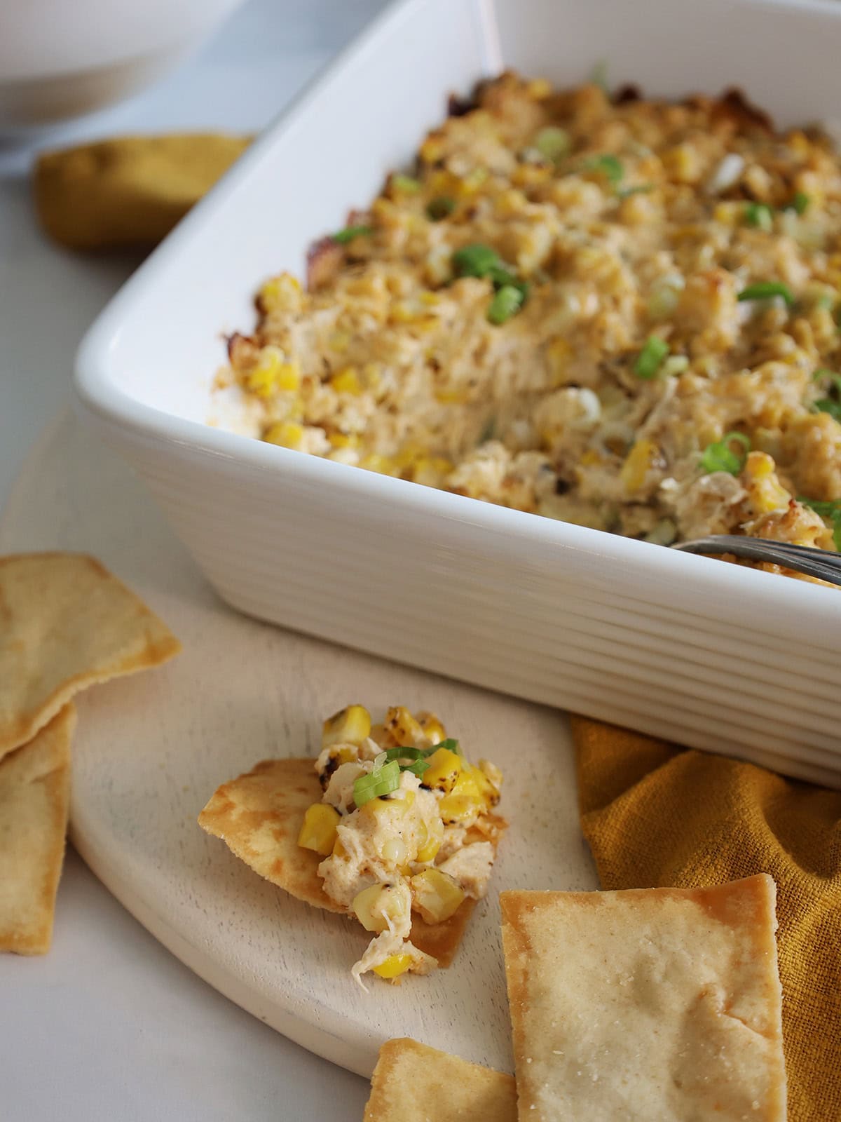 Crab dip on a pita chip with the rest of the dip in the background.