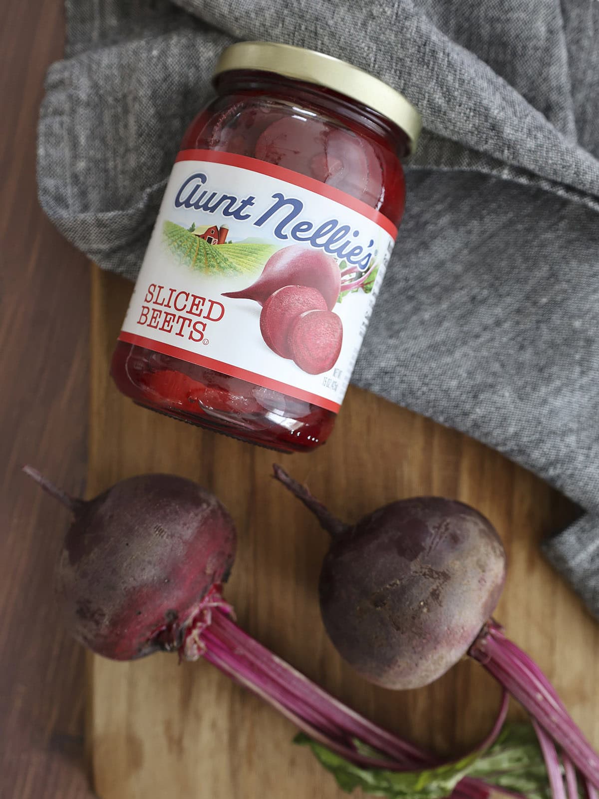 A jar of sliced beets next to two fresh beets.