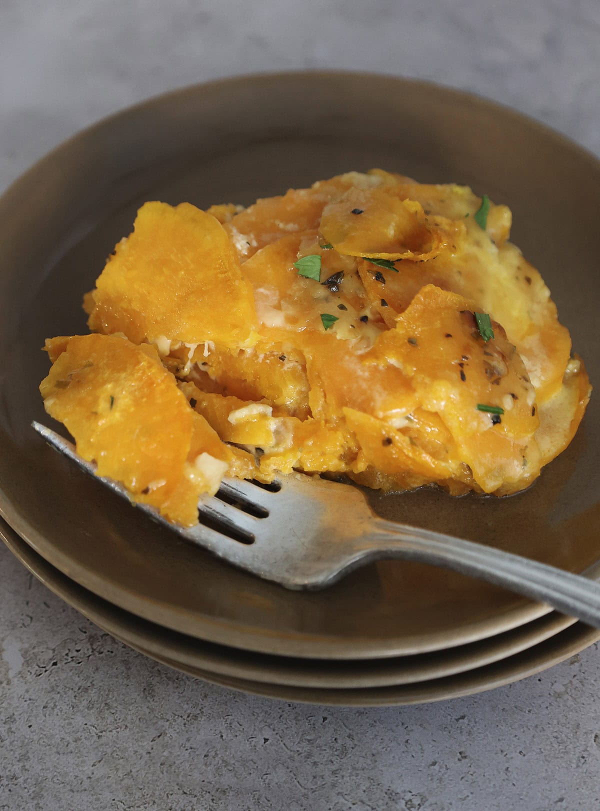 A serving of scalloped sweet potatoes on a plate with fork holding a bite.