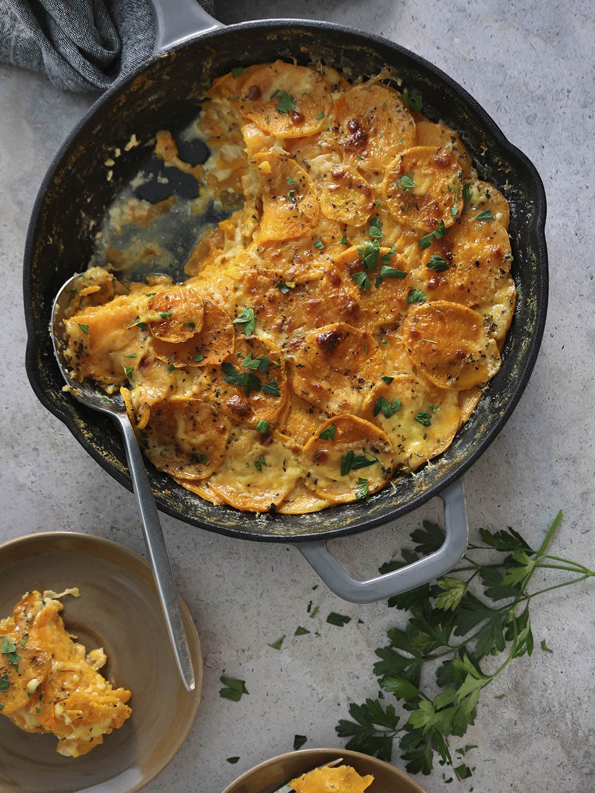 Top view of a skillet of scalloped sweet potatoes with a few portions removed by a spoon.