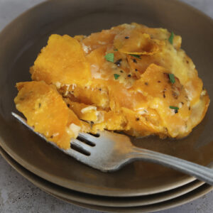 Close up of a serving of scalloped sweet potatoes with a bite on a fork.