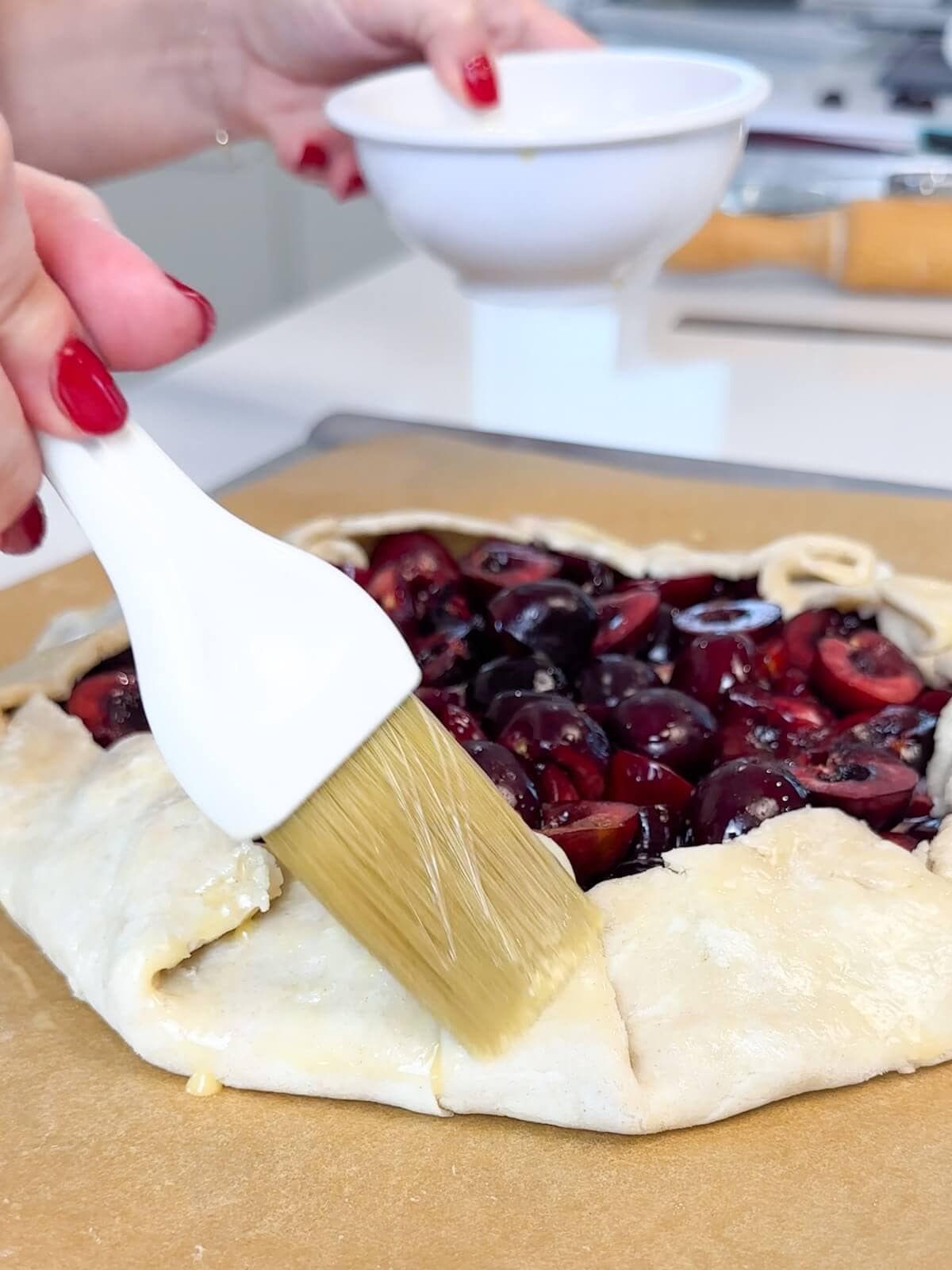 Brushing an egg wash around the outside of a cherry galette.