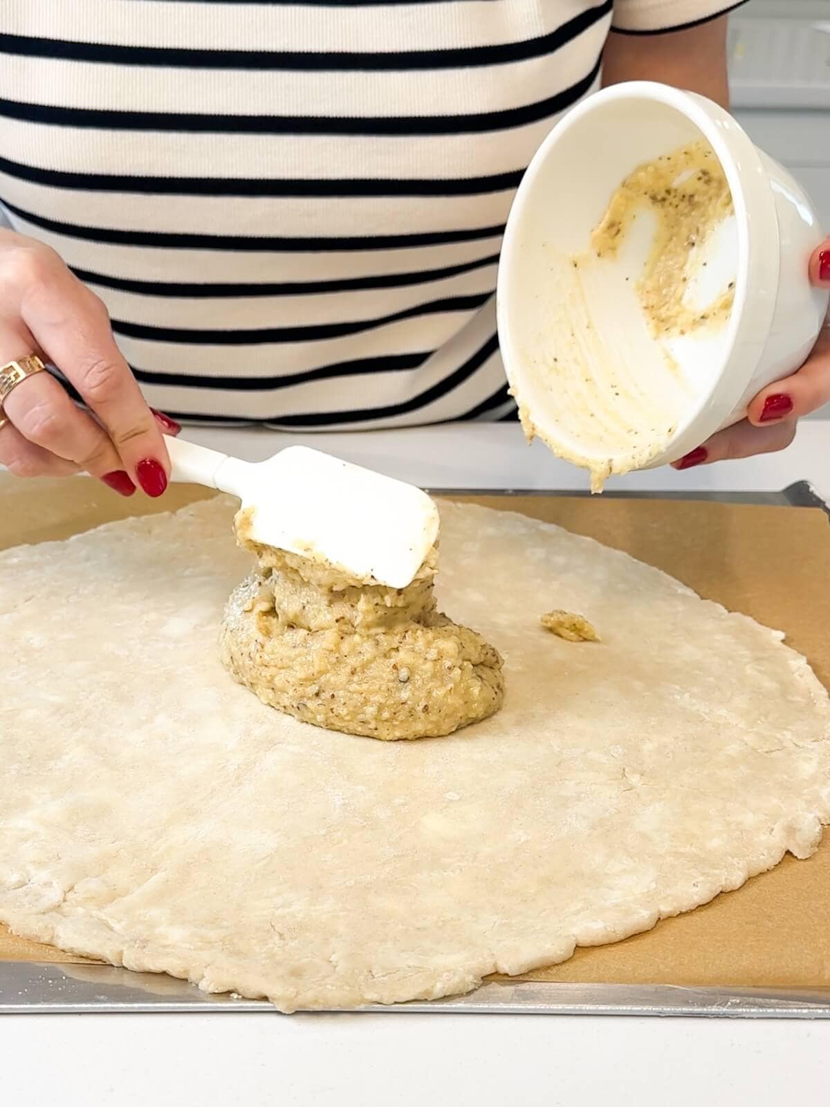 Using a spatula to spread frangipane in the center of rolled out pastry dough.