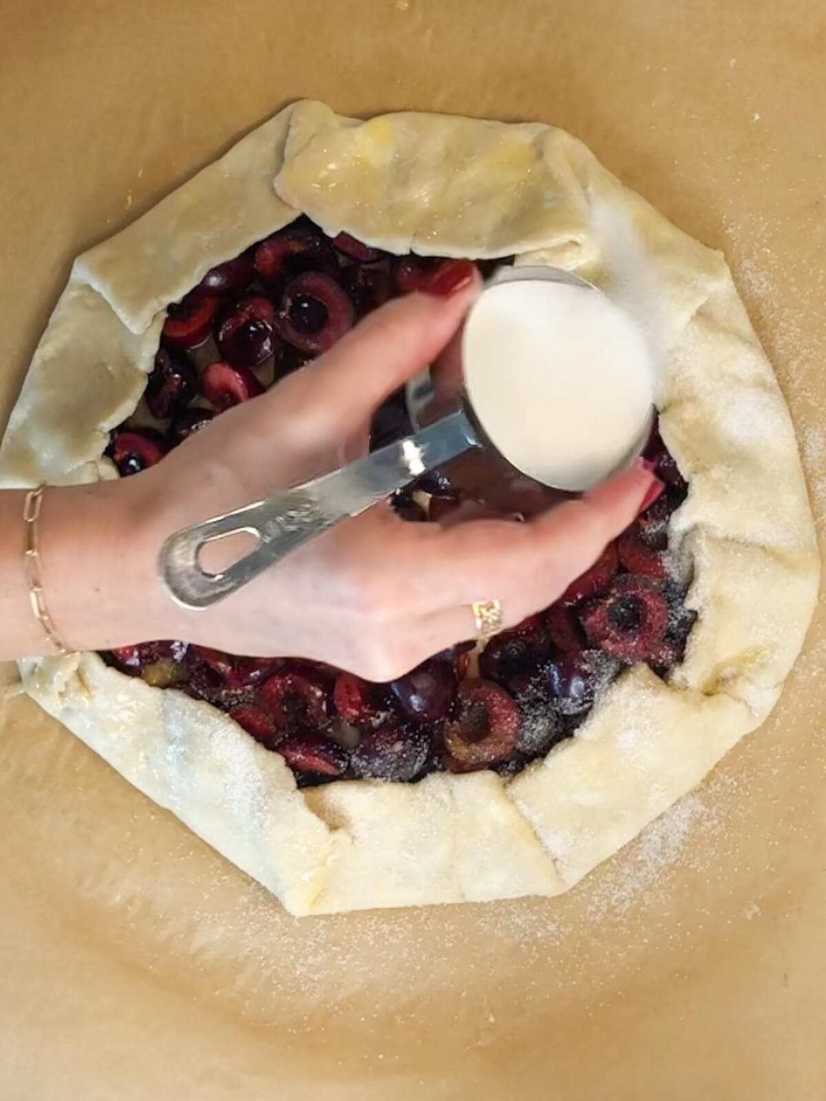 Hand sprinkling sugar around the outside of a cherry galette.